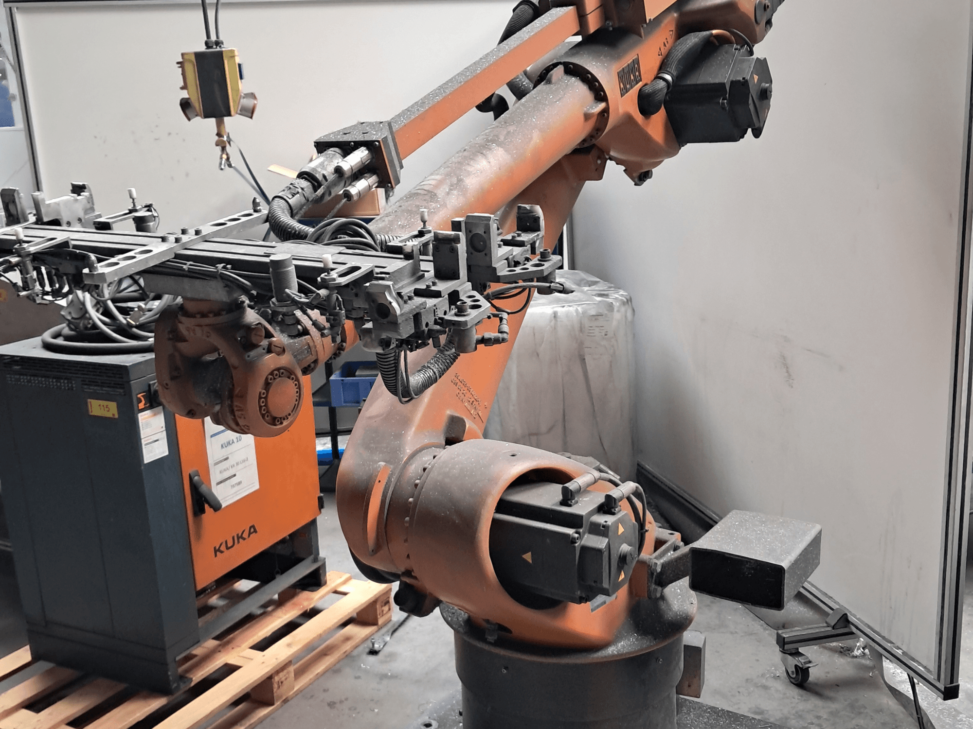 Bočni pogled na robotsku ruku KUKA KR 30L16-2, sa zamršenim krajnjim efektorom i upravljačkim kabelima, postavljenu pored KUKA upravljačke kutije.