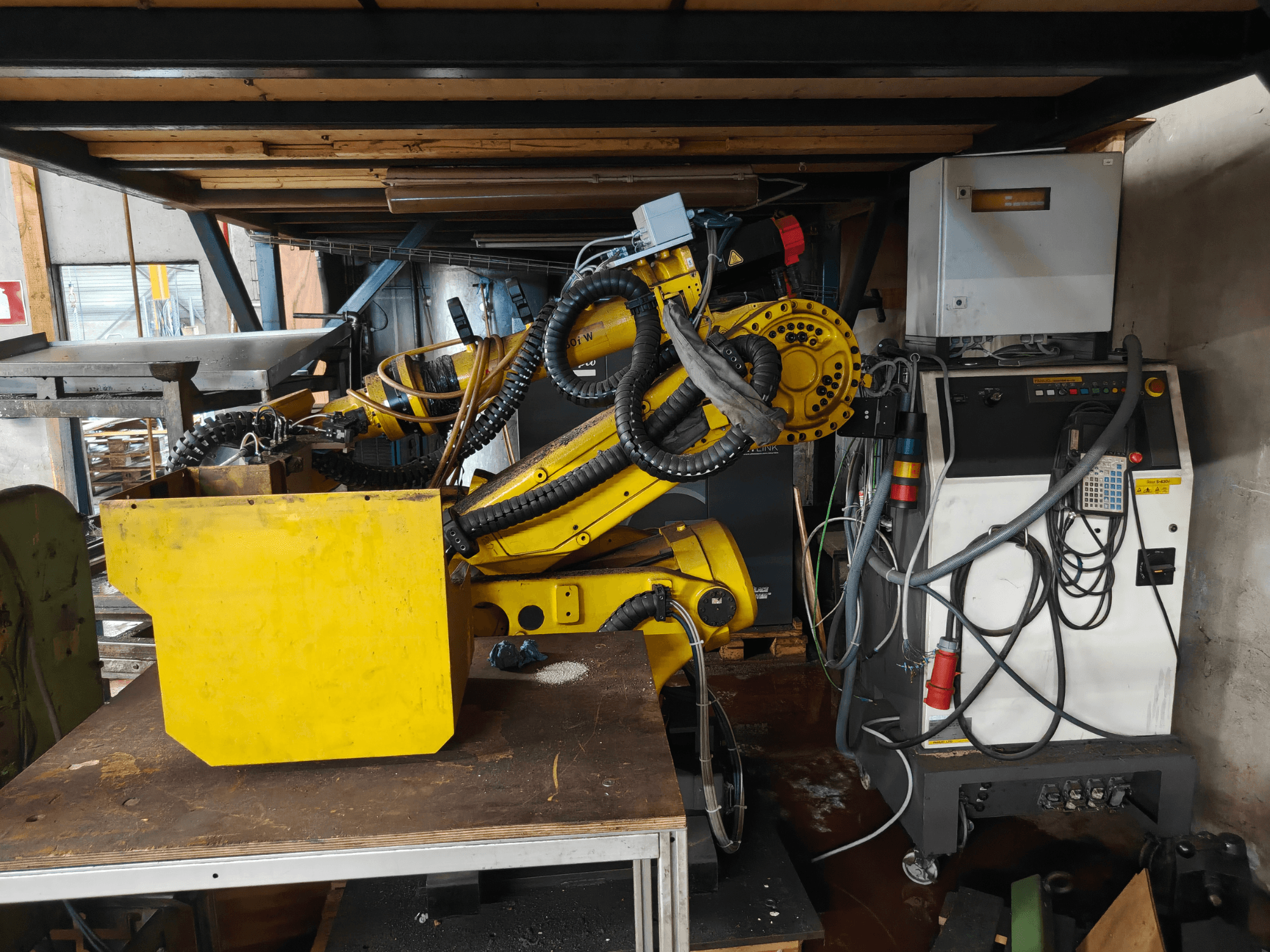 Prednji pogled na FANUC robotsku ruku S-430i W, žutu s upravljačkom pločom, kabelima i žutom komponentom na radnom stolu.