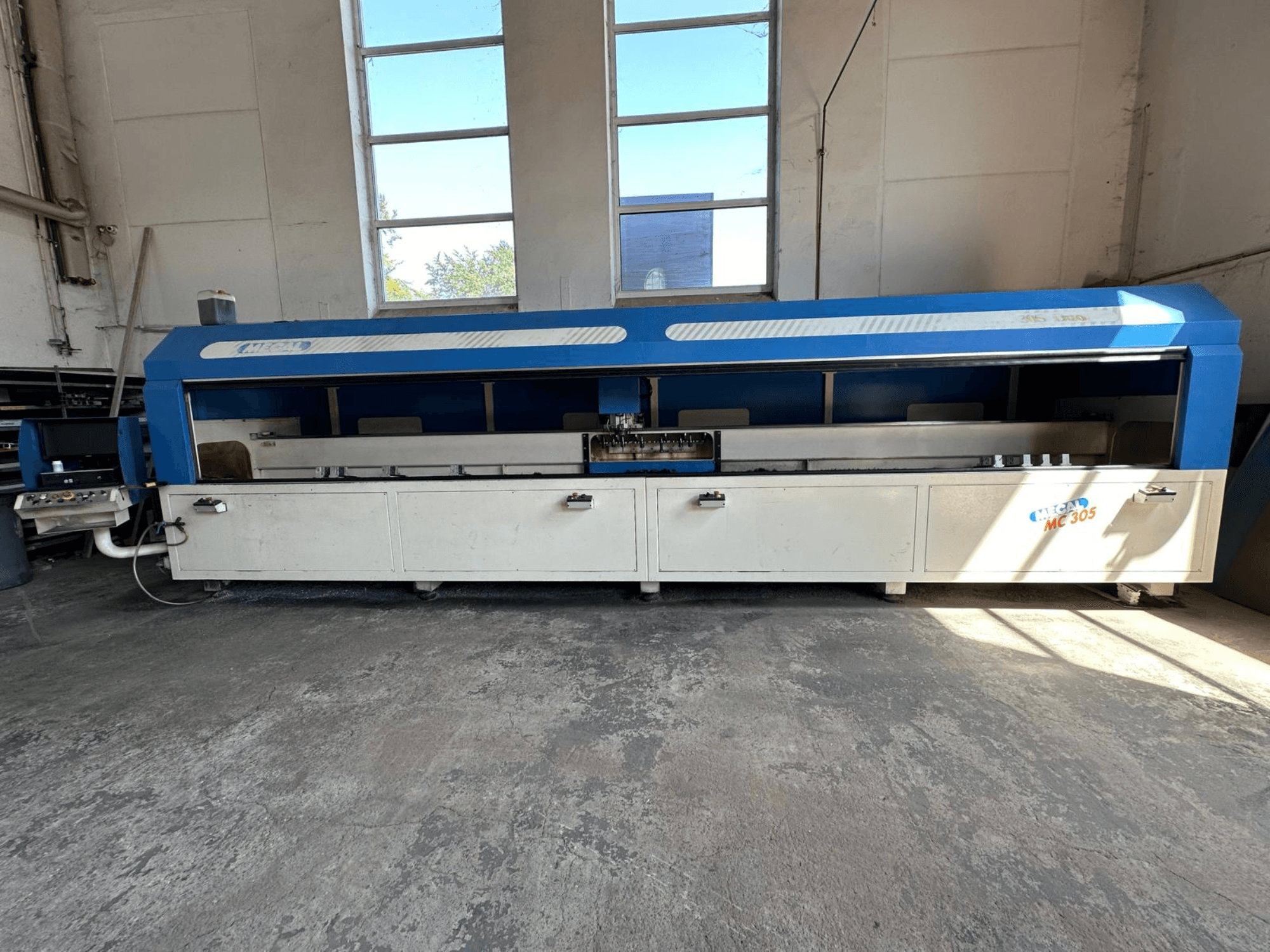 Prednji pogled na vertikalni obradni centar MECAL MC 305, plavo-bijelog dizajna, vidljivog radnog stola i upravljačke ploče.