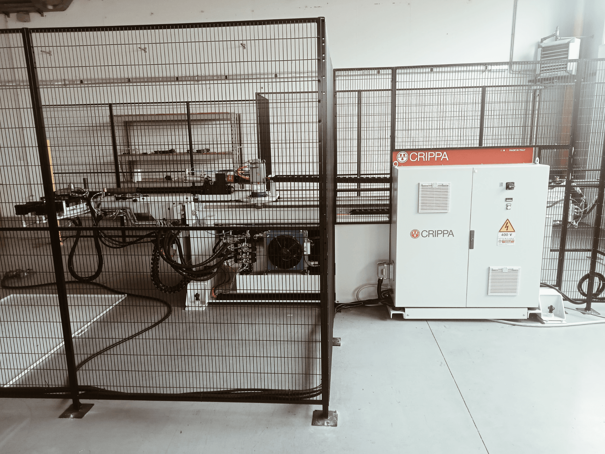 Bijeli CRIPPA stroj iza sigurnosnog kaveza, s vidljivim crijevima i komponentama, bočni pogled, industrijsko okruženje.