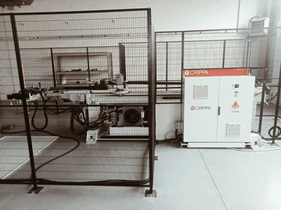 Bijeli CRIPPA stroj iza sigurnosnog kaveza, s vidljivim crijevima i komponentama, bočni pogled, industrijsko okruženje.