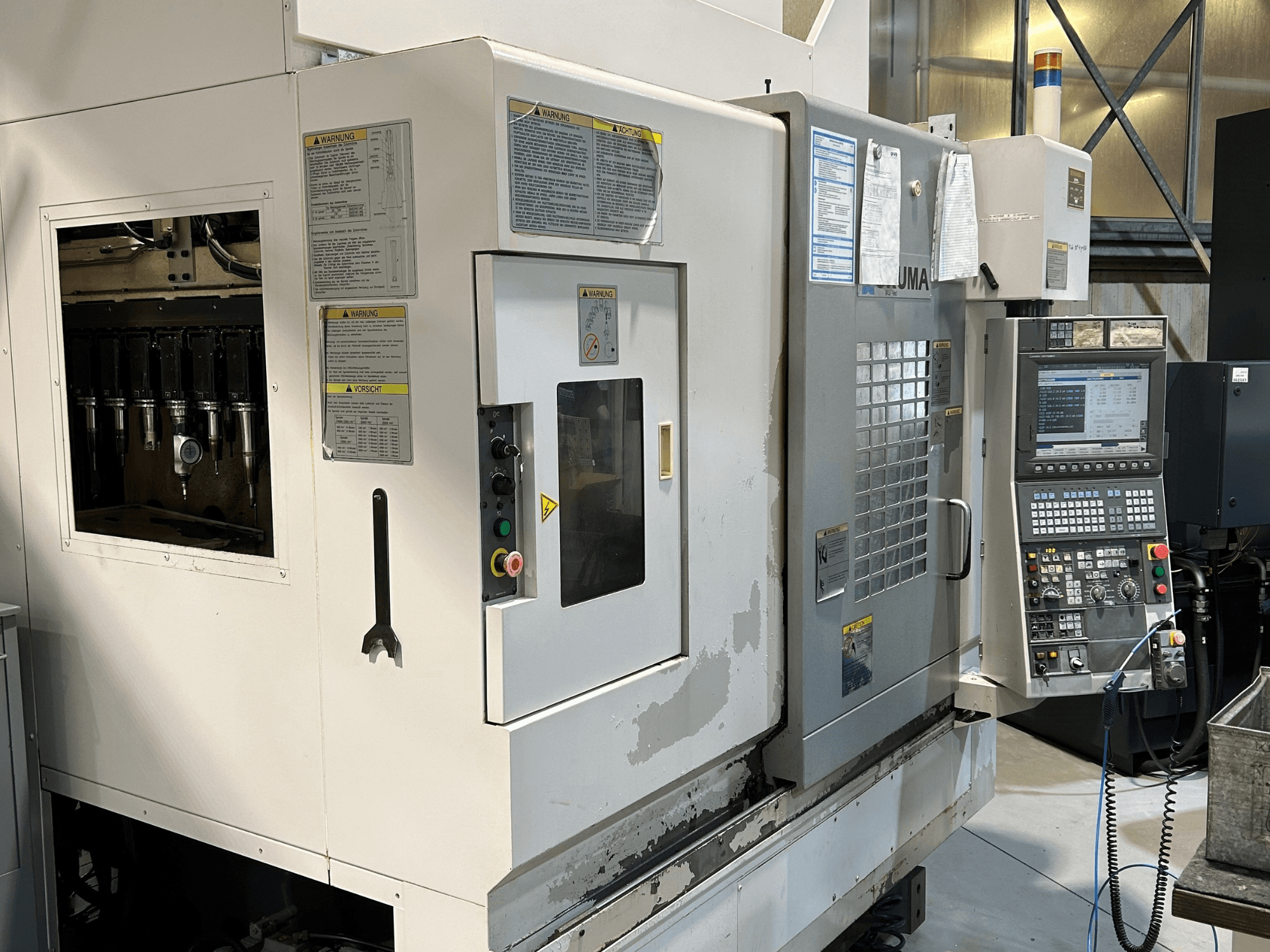Prednji pogled na UMA CNC stroj s vidljivim držačima alata, upravljačkom pločom, naljepnicama s upozorenjima i operativnim gumbima.