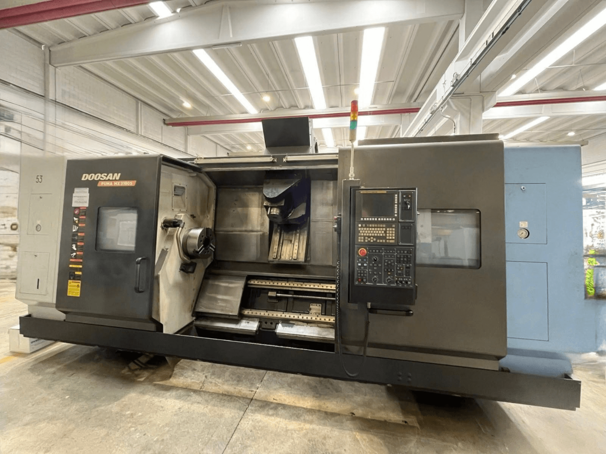 Prednji pogled na horizontalni tokarski stroj DOOSAN PUMA MX3100 s upravljačkom pločom i vidljivim područjem vretena i držača alata.