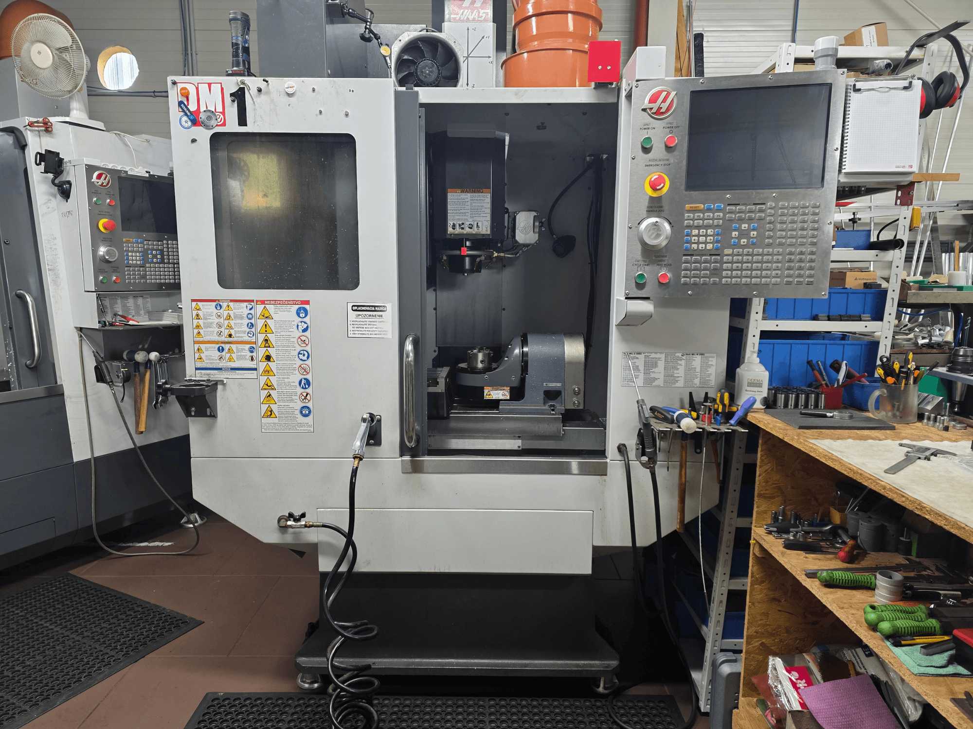 Haas CNC stroj model VF-2, pogled sprijeda, prikazuje kontrole, područje vretena, sigurnosne naljepnice i alate na obližnjem radnom stolu.