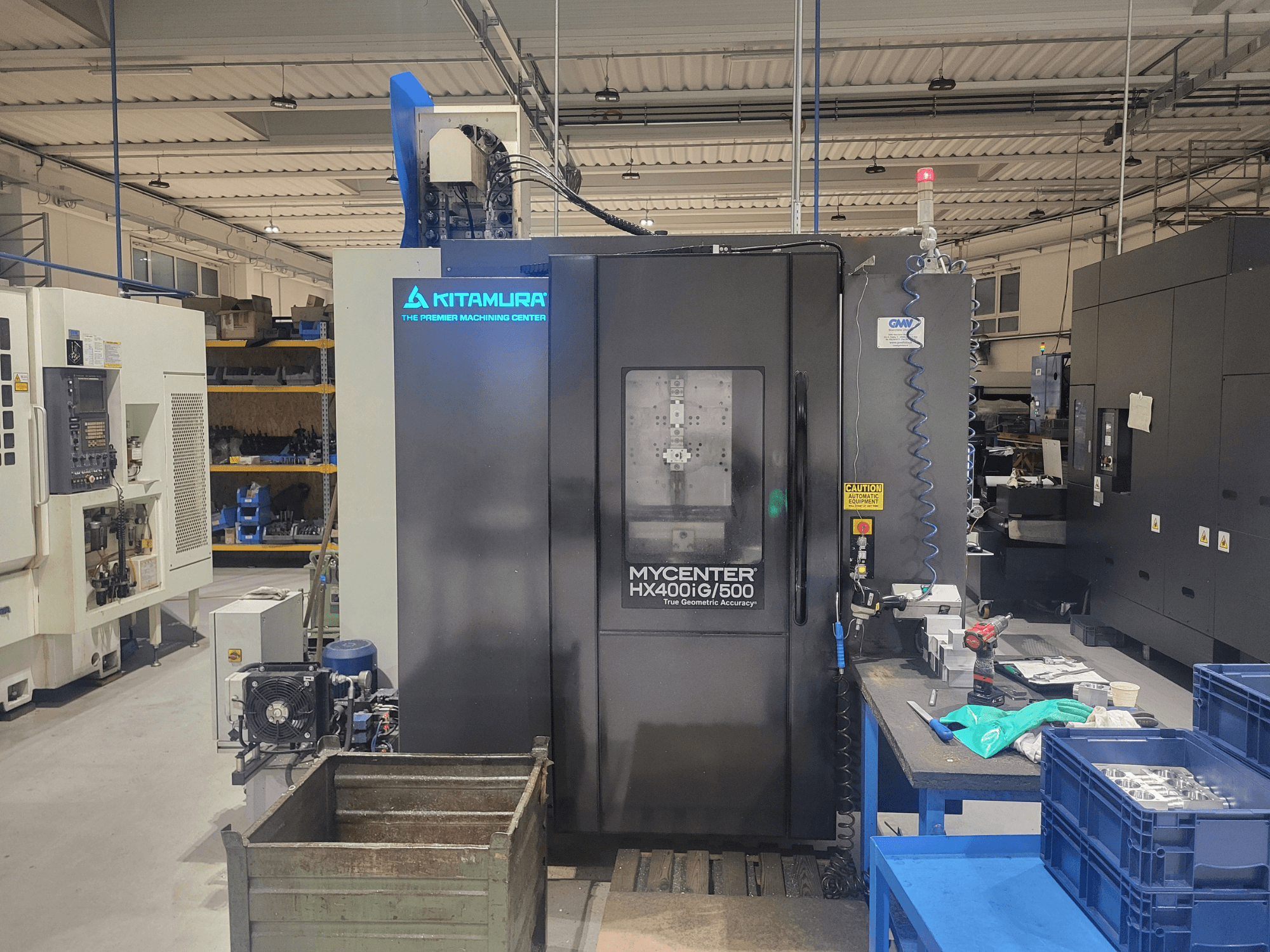 Kitamura Mycenter HX400iG/500 CNC stroj u radionici, pogled sprijeda, s upravljačkim elementima, skladištem alata i materijalima u blizini.