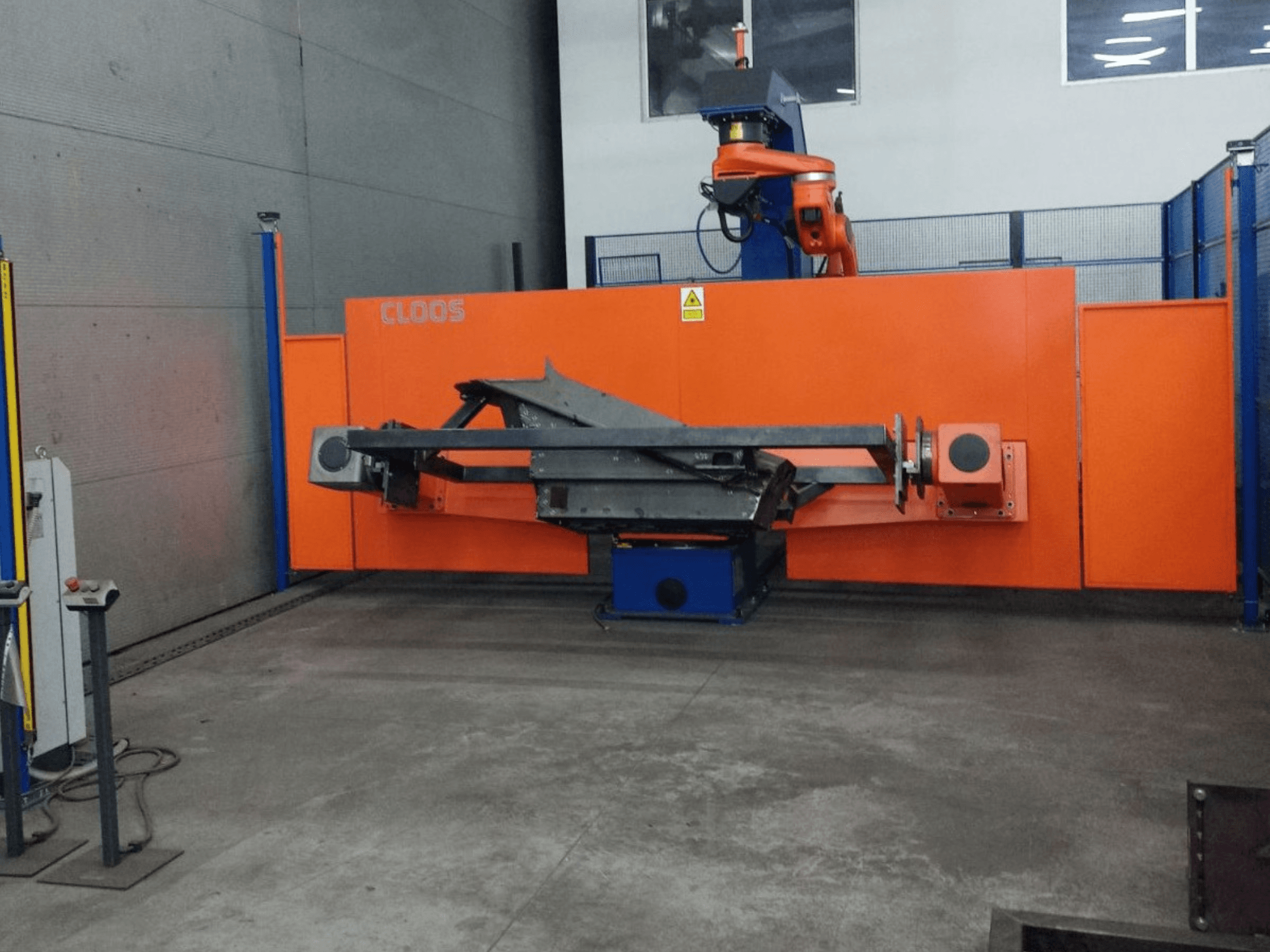 Prednji pogled na CLOOS QIROX QRC-350-E automatizacijski sustav s robotskom rukom i metalnom konstrukcijom u industrijskom okruženju.