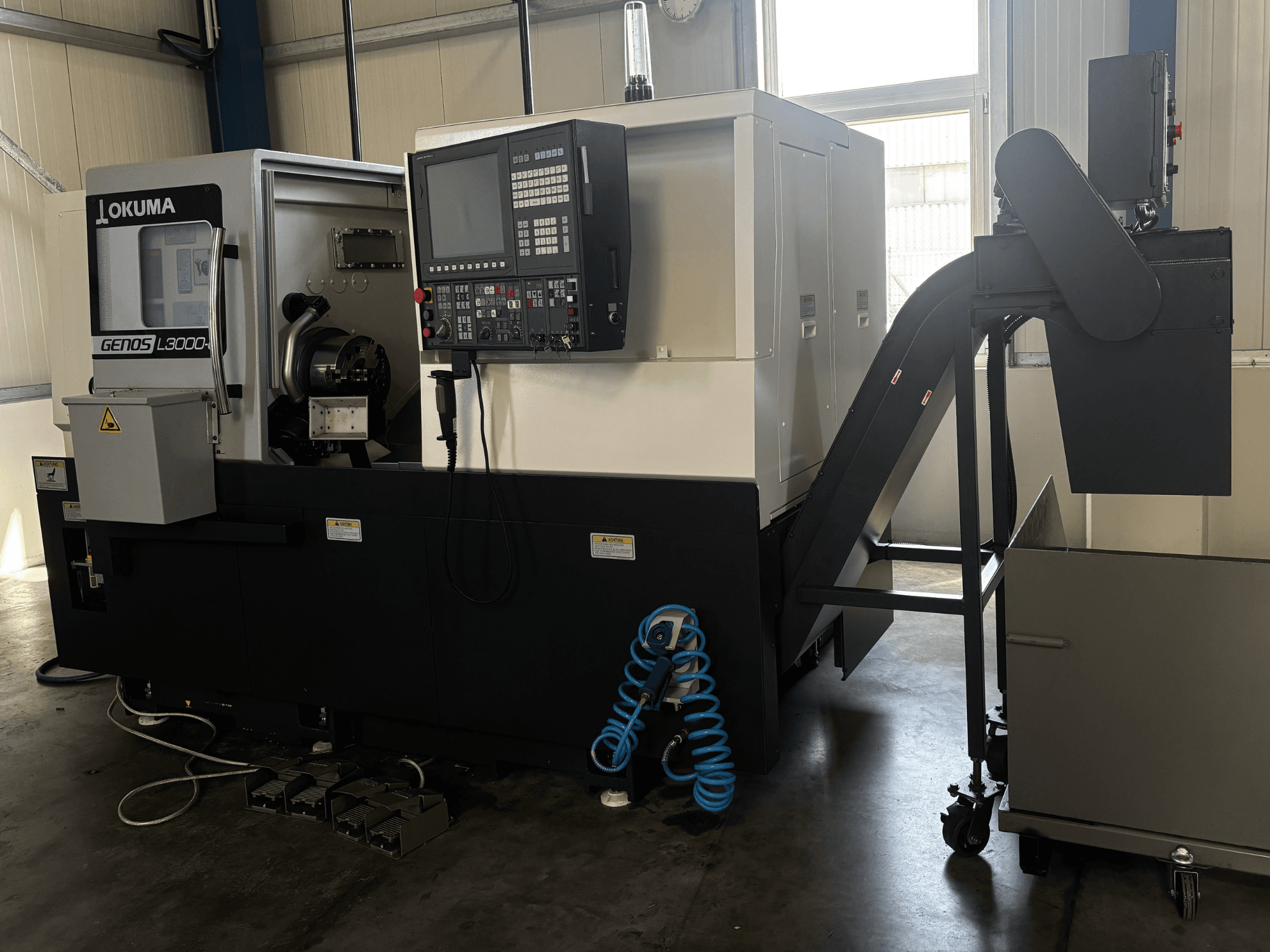 Okuma GENOS L3000-e horizontalni tokarski stroj, prednji pogled, sadrži upravljačku ploču, transporter i vidljivo područje vretena.