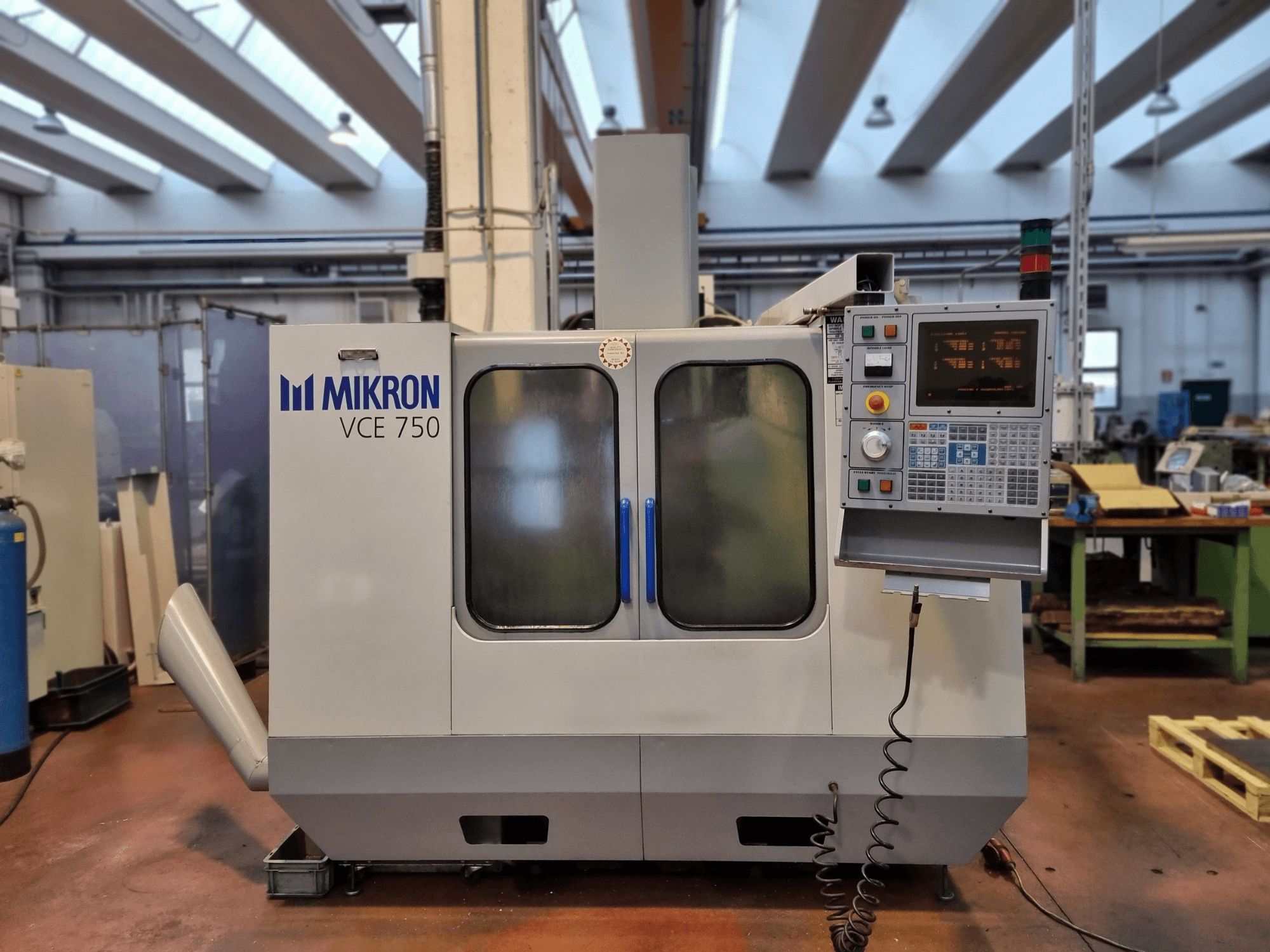 Bijeli Mikron VCE 750 CNC stroj u radionici, bočni pogled, s digitalnom upravljačkom pločom i velikim staklenim vratima.