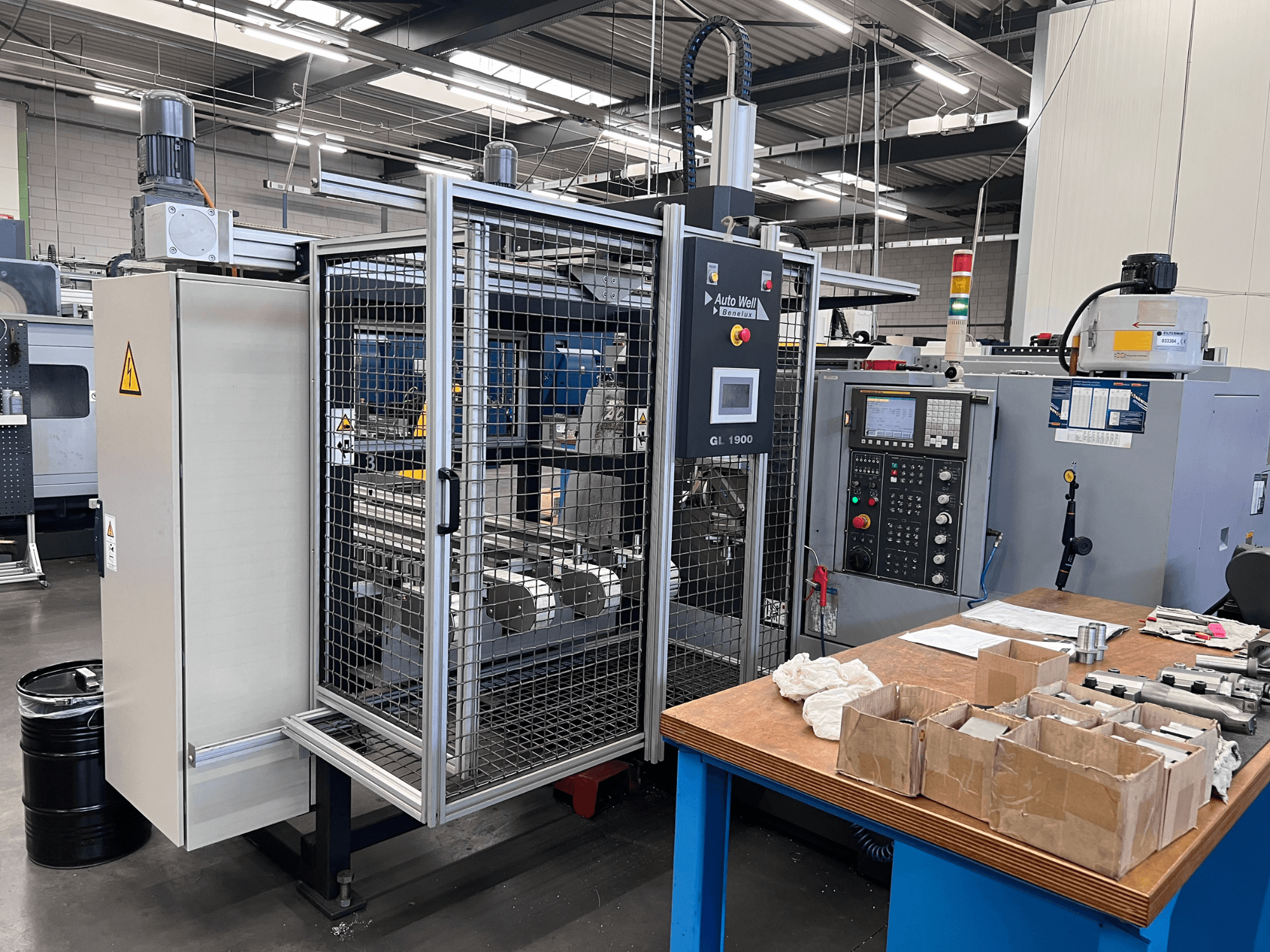 Prednji pogled na stroj Auto Weld GL 1900 s upravljačkom pločom, sigurnosnim kućištem i okolnim alatima na radnom stolu.