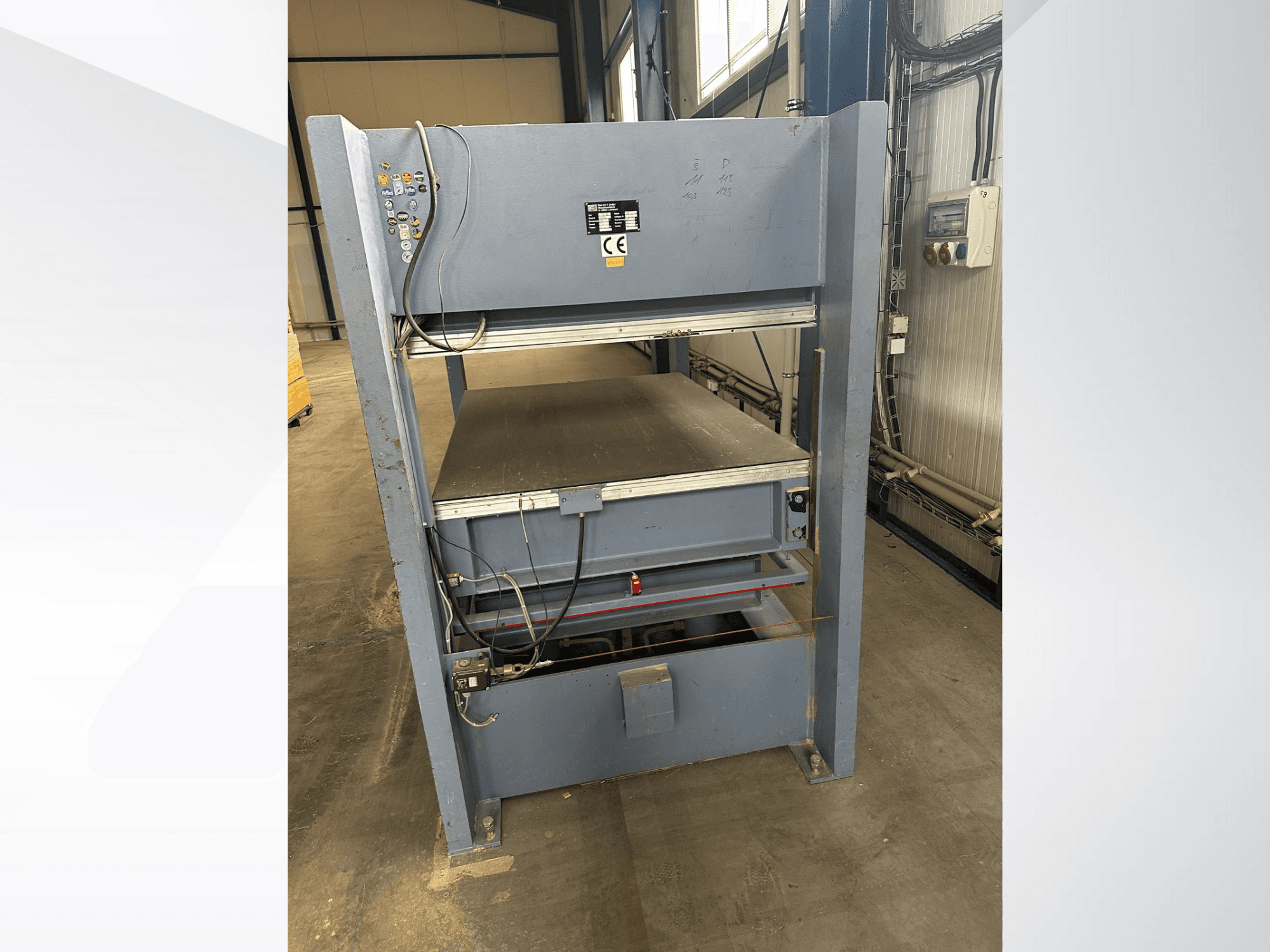 Sivi industrijski stroj s upravljačkom pločom, gledano sprijeda; uključuje podesive platforme i sigurnosne oznake.