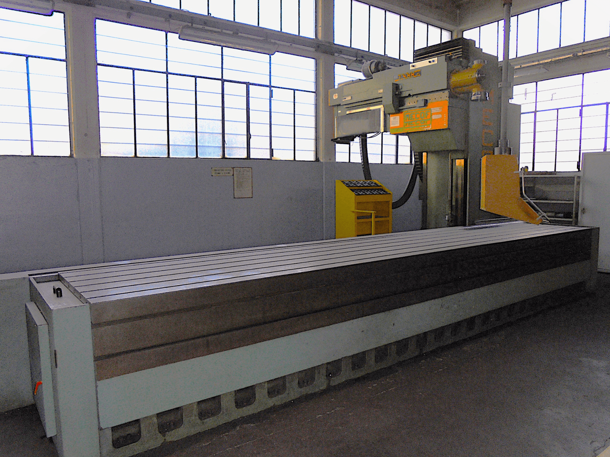 Vertikalna glodalica nepoznate marke u tvornici, bočni pogled, ima veliki stol s utorima i upravljačku ploču.