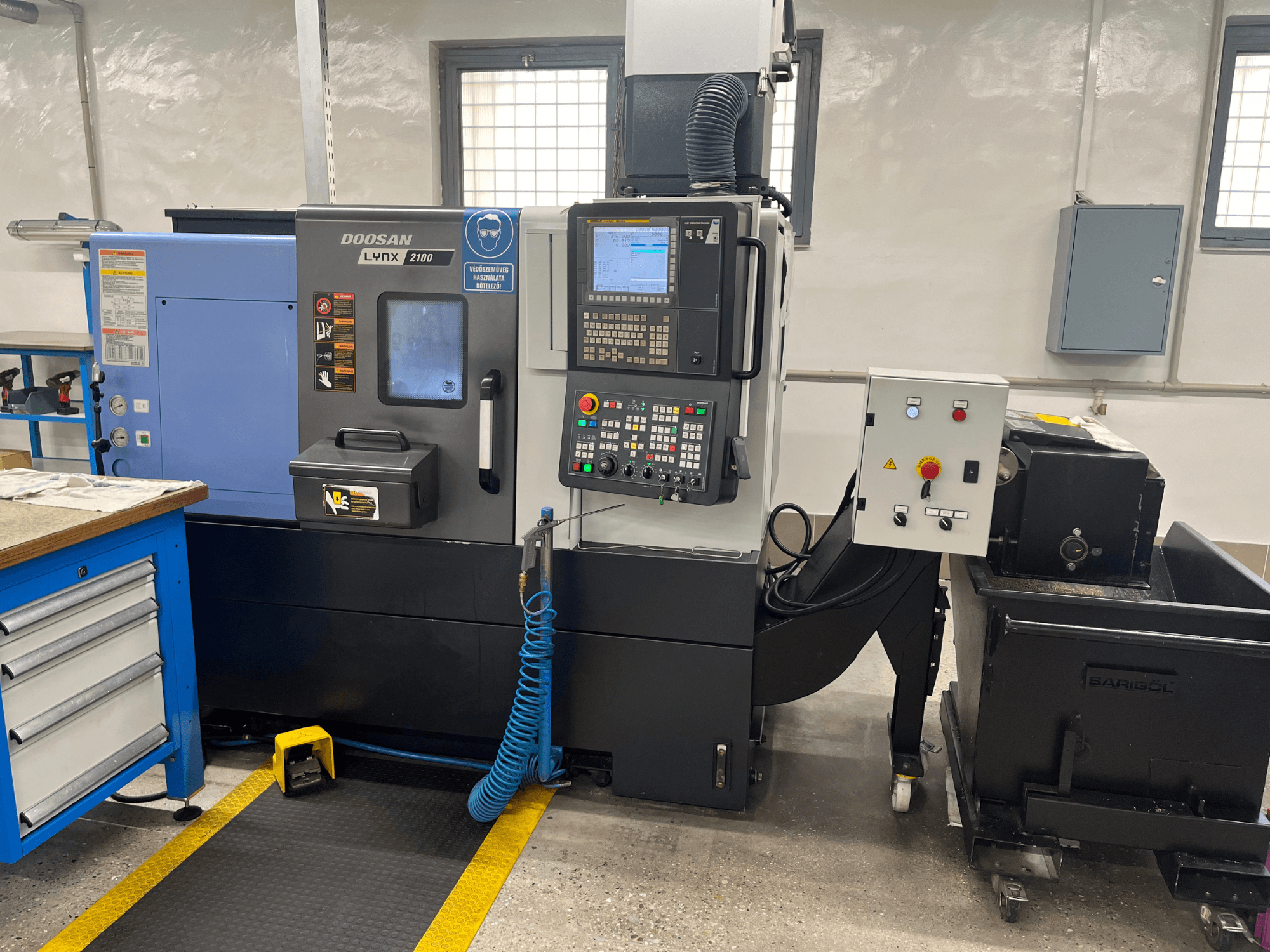 Tokarski stroj Doosan Lynx 210 u radionici, s prikazom upravljačke ploče, spremišta alata i sustava za hlađenje, bočni pogled s detaljima radnog prostora.