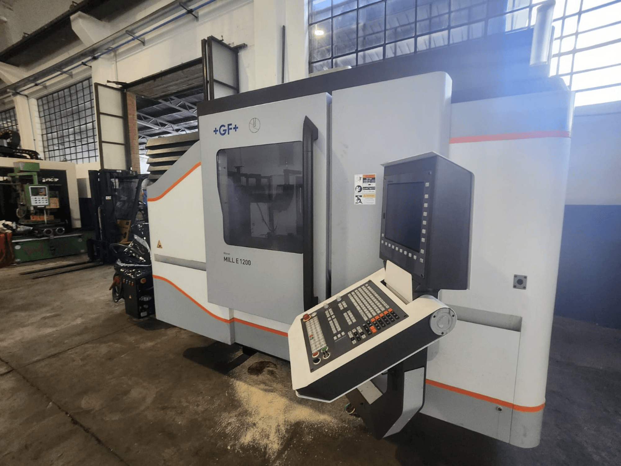 GF MILL E1200, prednji pogled na glodalicu s upravljačkom pločom, zaslonom i sigurnosnim naljepnicama, u radioničkom okruženju.