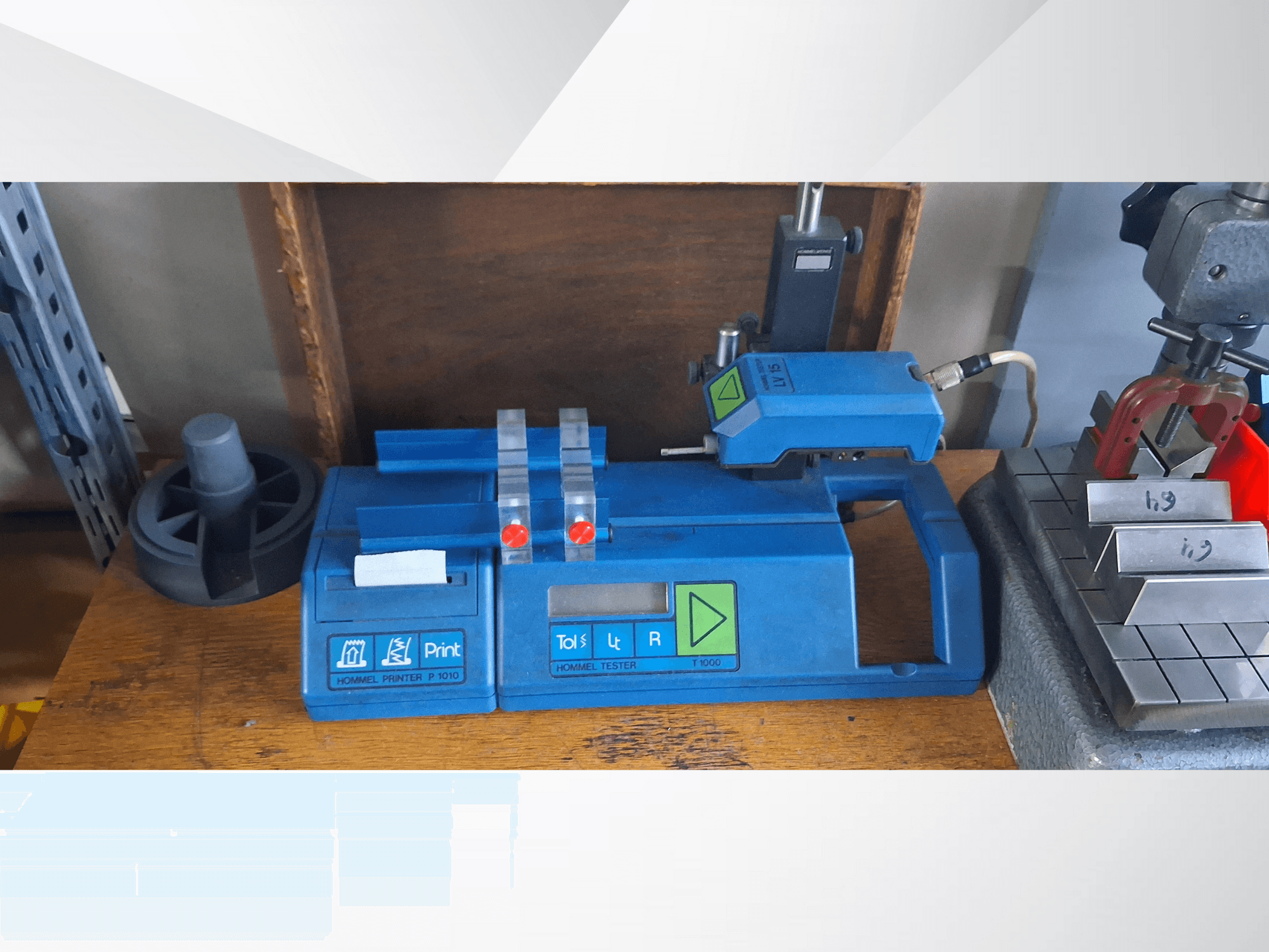 Plavi pisač Hommel T 1000 i tester T 1010 s crvenim gumbima, gledano sprijeda na radnom stolu s metalnim blokovima.