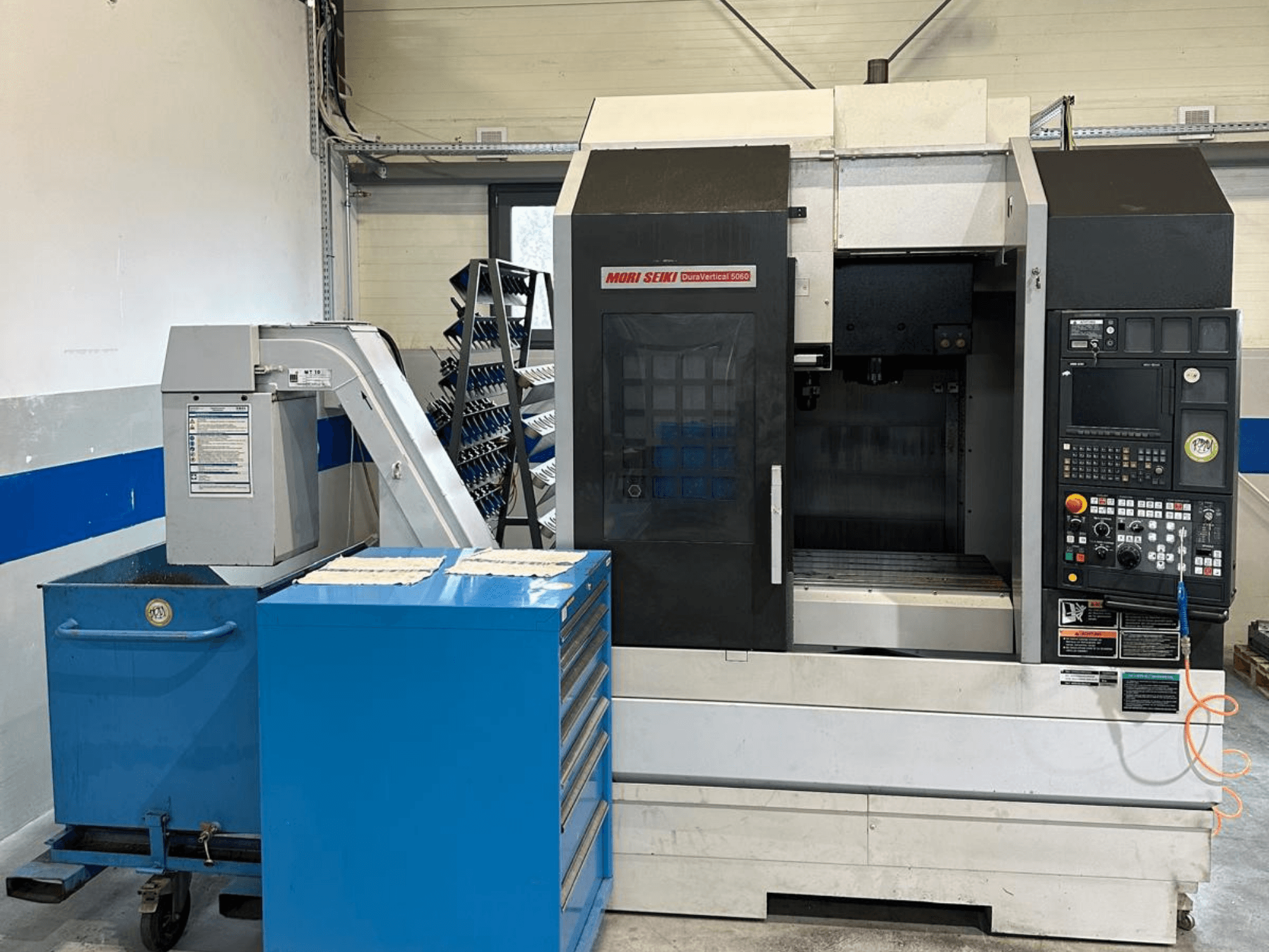 MORI SEIKI DURA VERTICAL 5060, prednji pogled na vertikalni obradni centar s upravljačkom pločom i obližnjim skladištem alata.