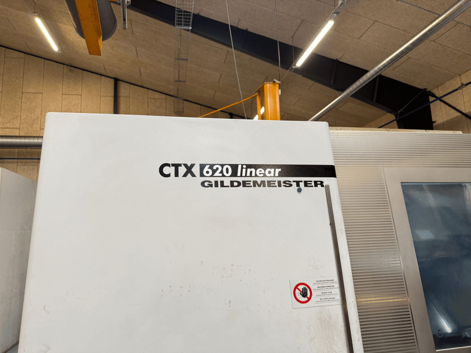 Bočni prikaz stroja CTX 620 Linear Gildemeister, s bijelom vanjštinom i sigurnosnim upozorenjima.