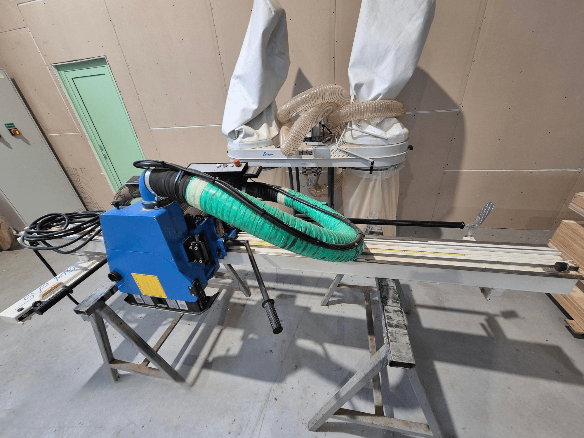 Plava horizontalna pila za ploče SVP-175 sa zelenim crijevom za prašinu i nosačem, gledano sa strane u radioničkom okruženju.