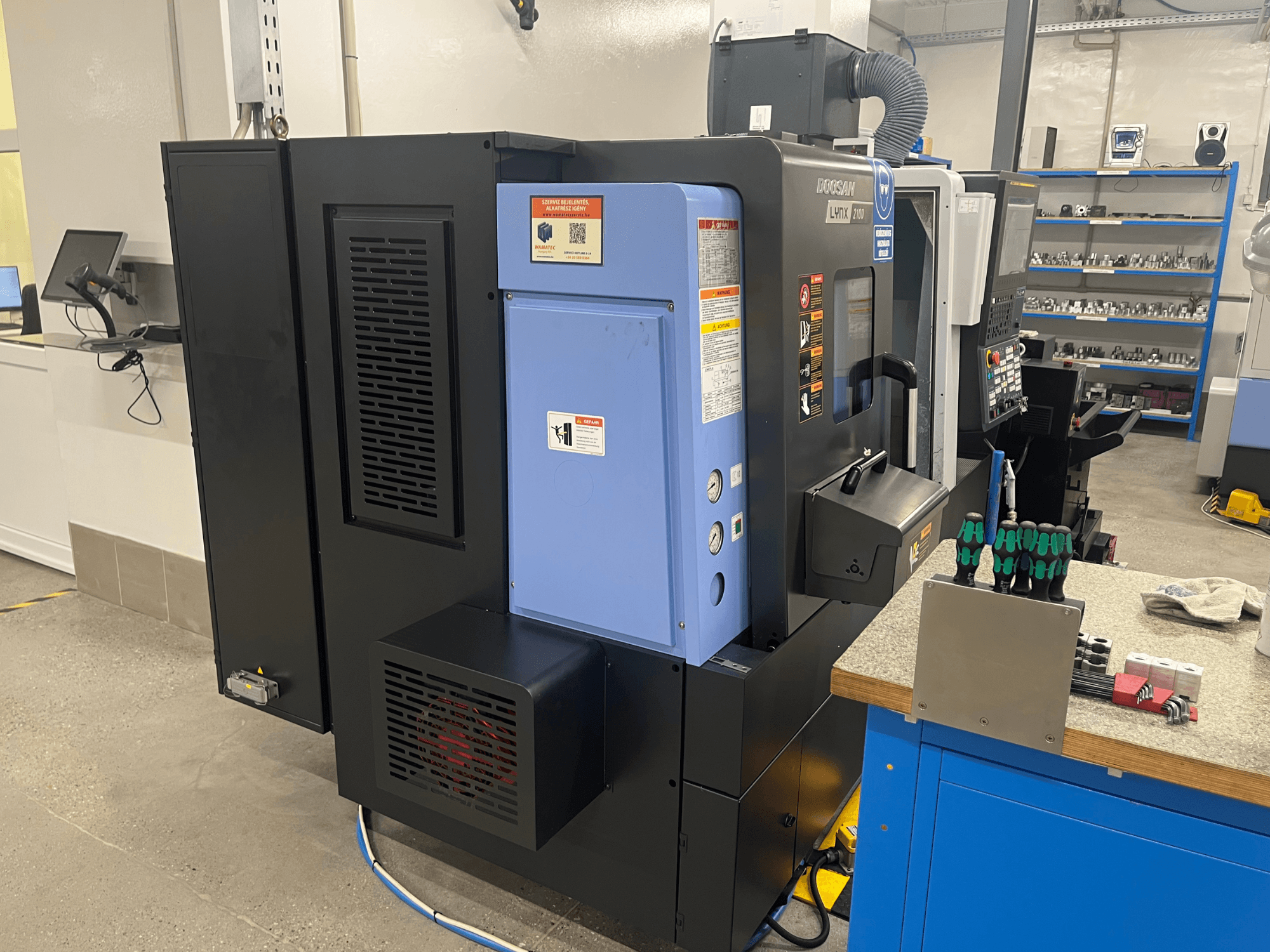 Tokarski stroj Doosan Lynx 2100, bočni pogled, prikazuje upravljačku ploču, ventilacijski sustav i alate na radnom stolu.