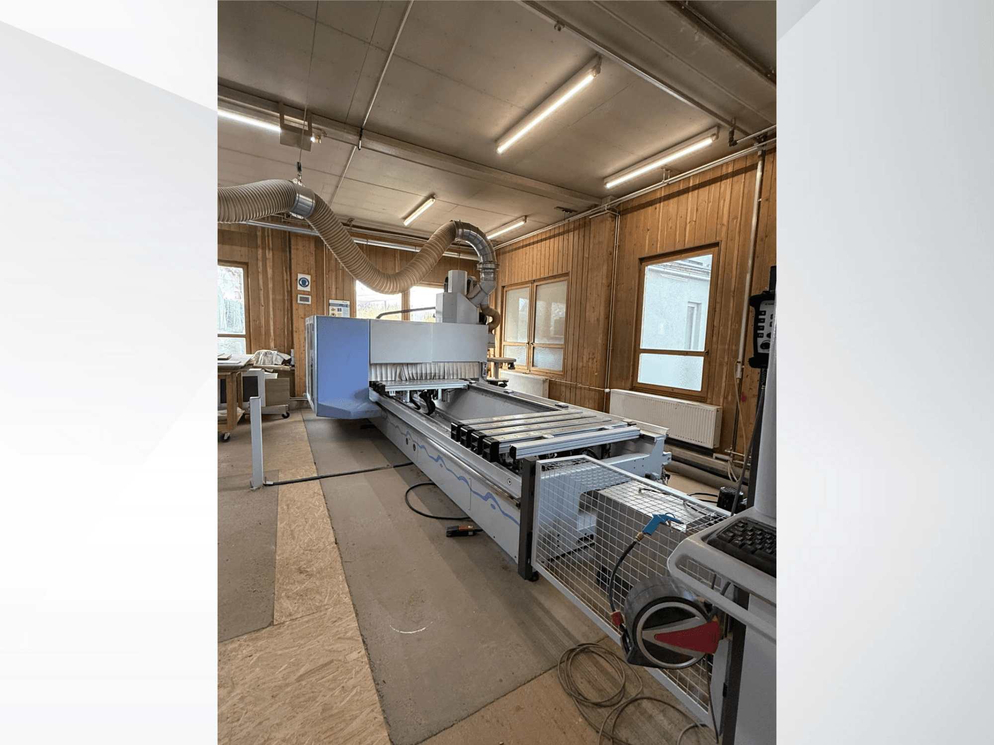 CNC glodalica u radionici, bočni pogled, s velikim plavim tijelom, pričvršćenom trakastom transportnom trakom i vidljivom upravljačkom pločom.