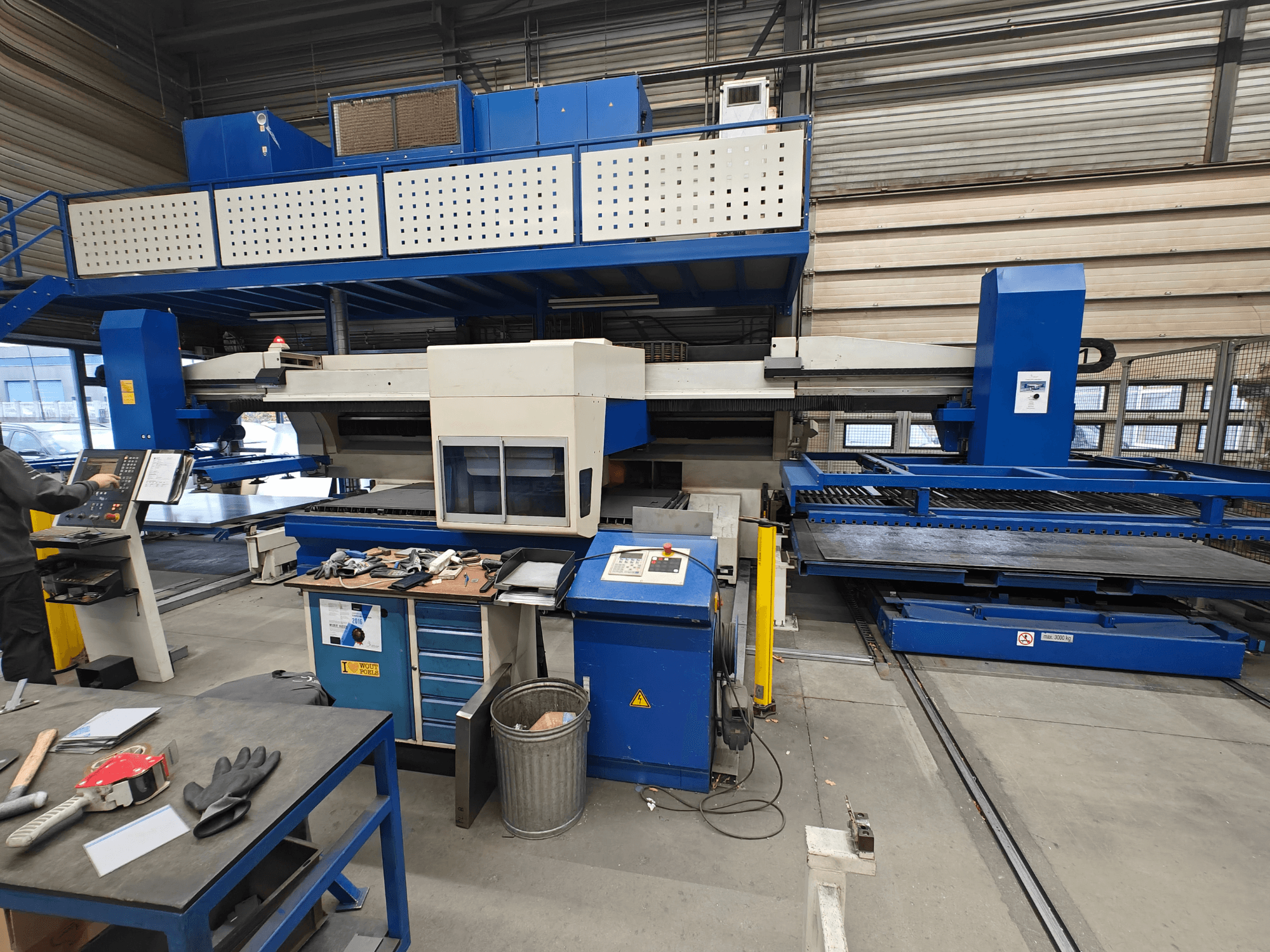 Industrijski CNC stroj s prednje strane, s plavo-bijelom konstrukcijom, upravljačkom pločom i raznim alatima na radnom stolu.