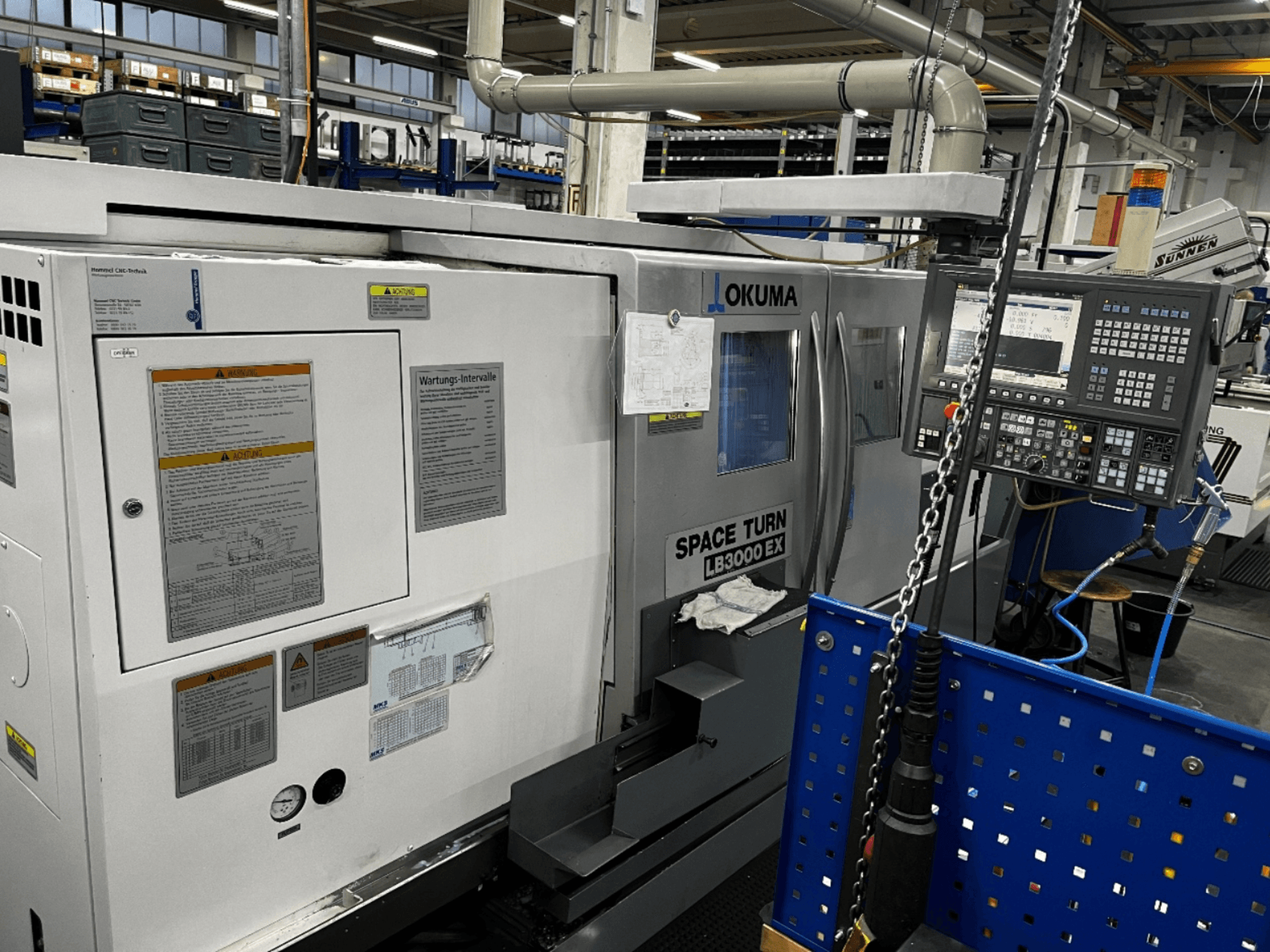 Horizontalni tokarski stroj Okuma LB3000 EX, prednji pogled, prikaz upravljačke ploče i sigurnosnih informacija sa strane.