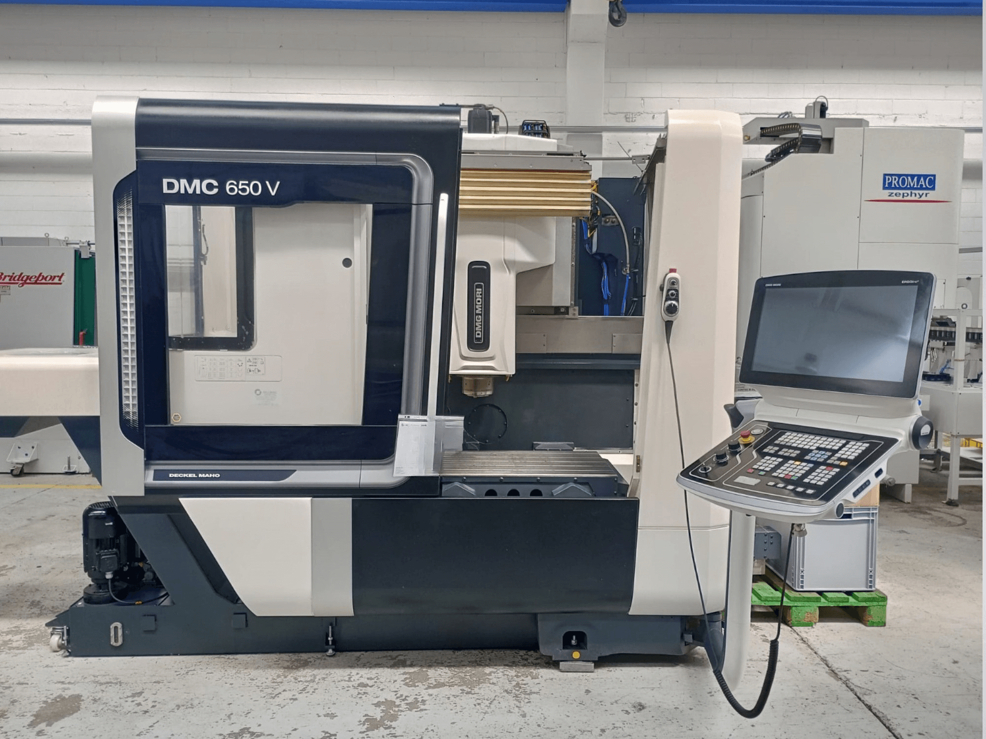 Bočni prikaz CNC stroja Decker Maho DMC 650 V, s upravljačkom pločom s gumbima i zaslonom, u industrijskom okruženju.