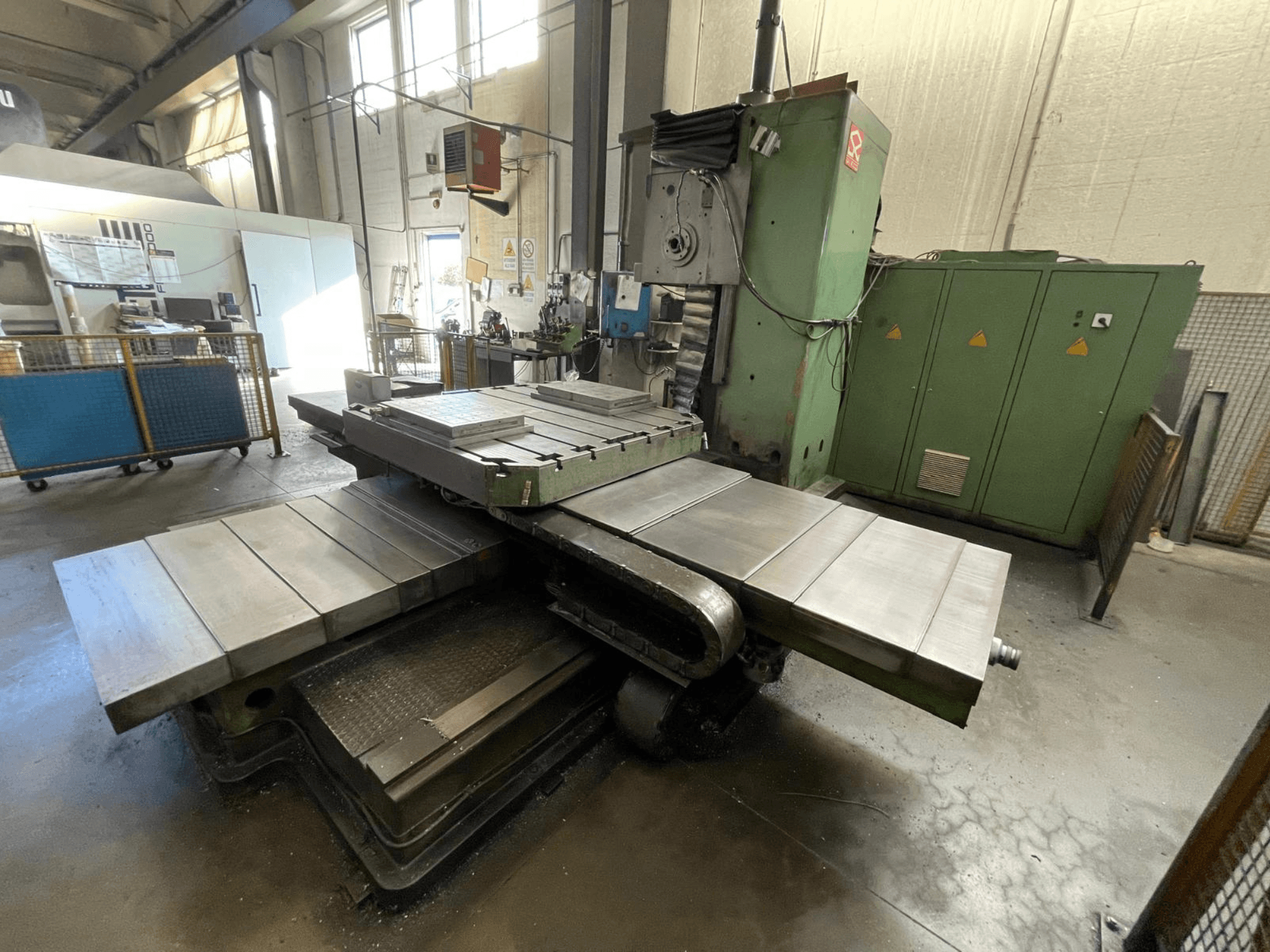 Velika industrijska glodalica sa zelenim tijelom, bočni pogled, s više ravnih površina i ormarićima za pohranu u pozadini.