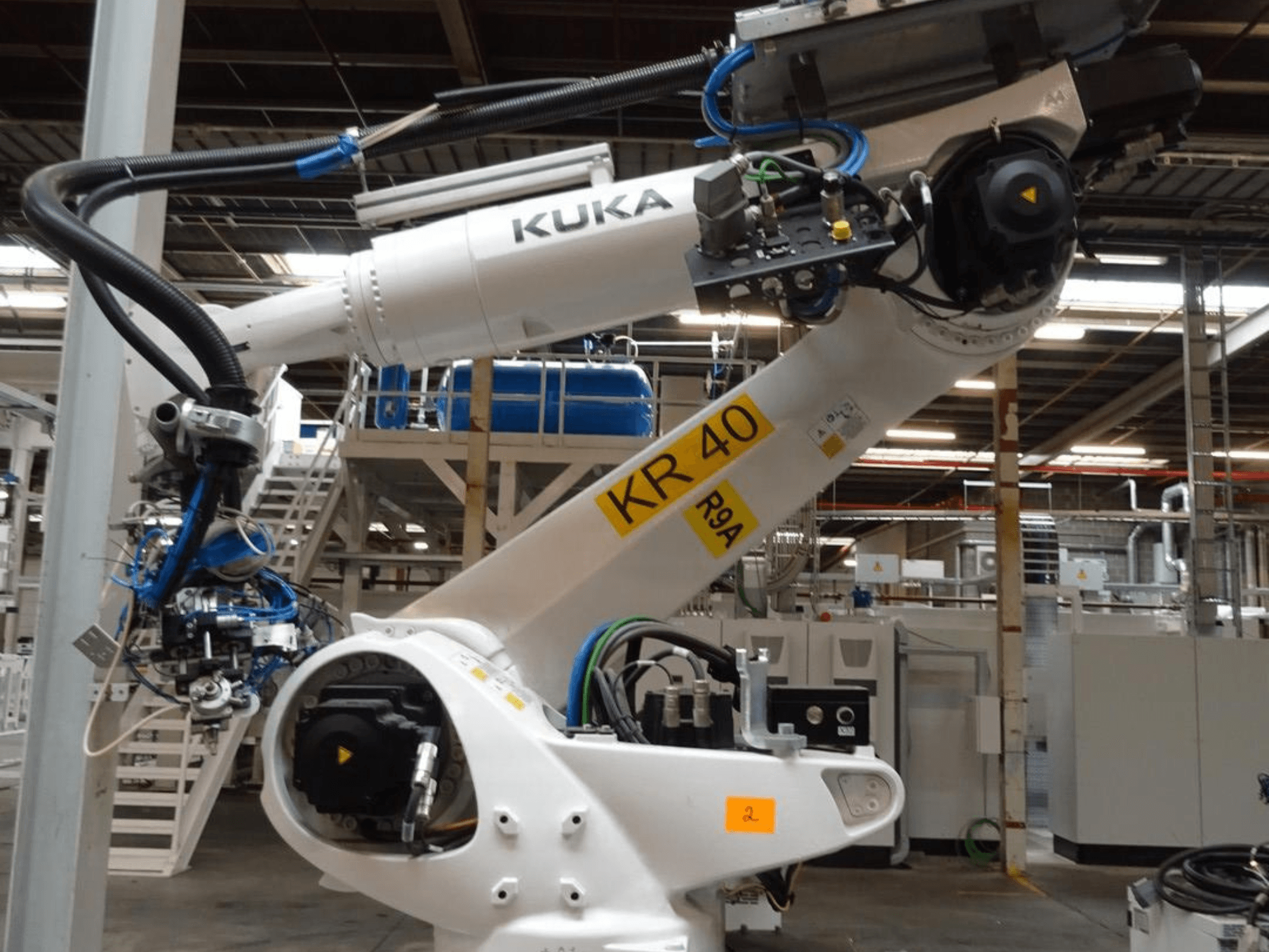 Bočni pogled na robotsku ruku KUKA KR 120 R3100-2, s upravljačkom pločom i mehaničkim komponentama, smještenu u industrijskom okruženju.