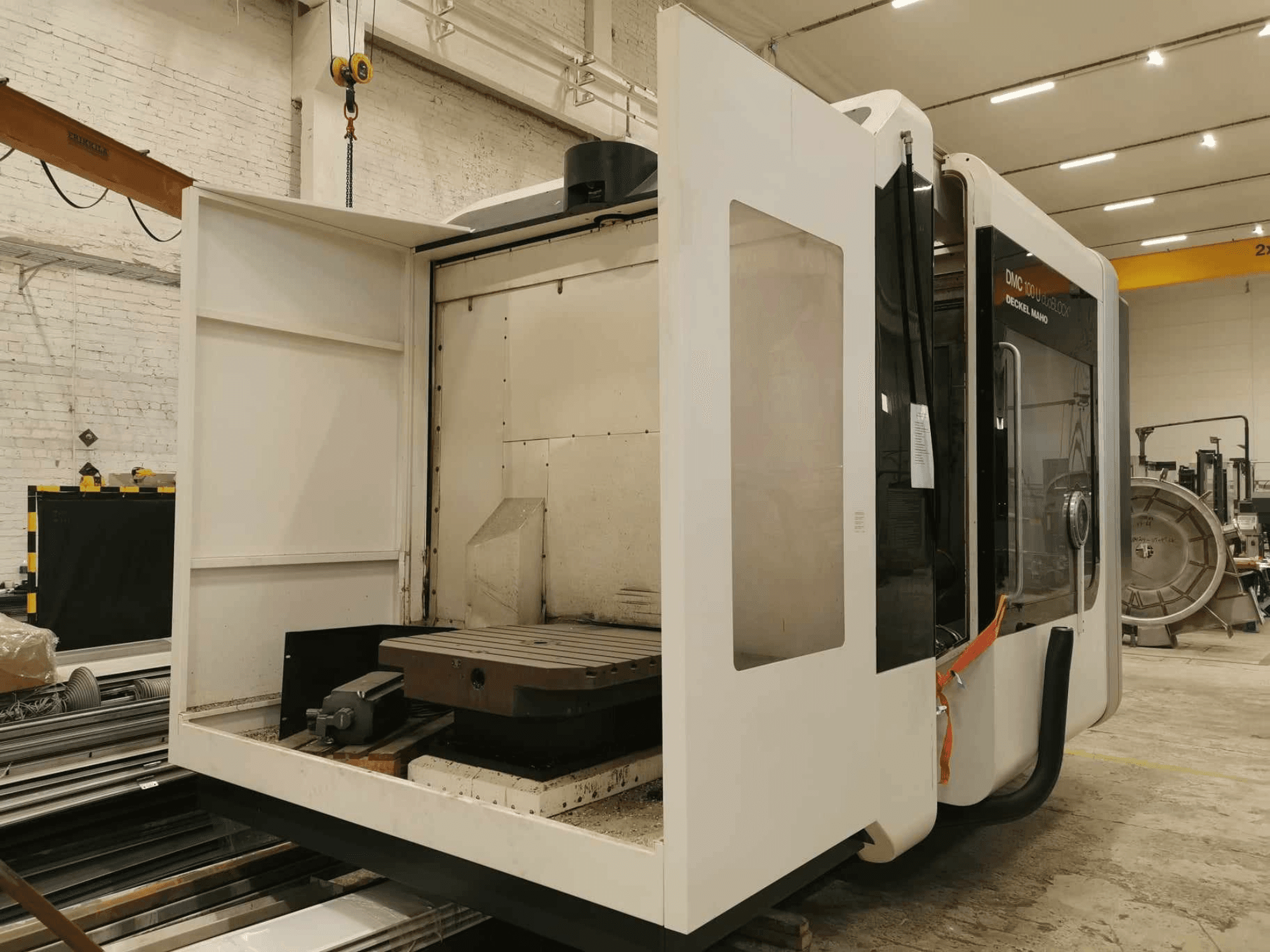 Linearni CNC stroj DMC 100U, bočni pogled s otvorenim vratima za pristup, prikazuje radni stol i unutarnje komponente.
