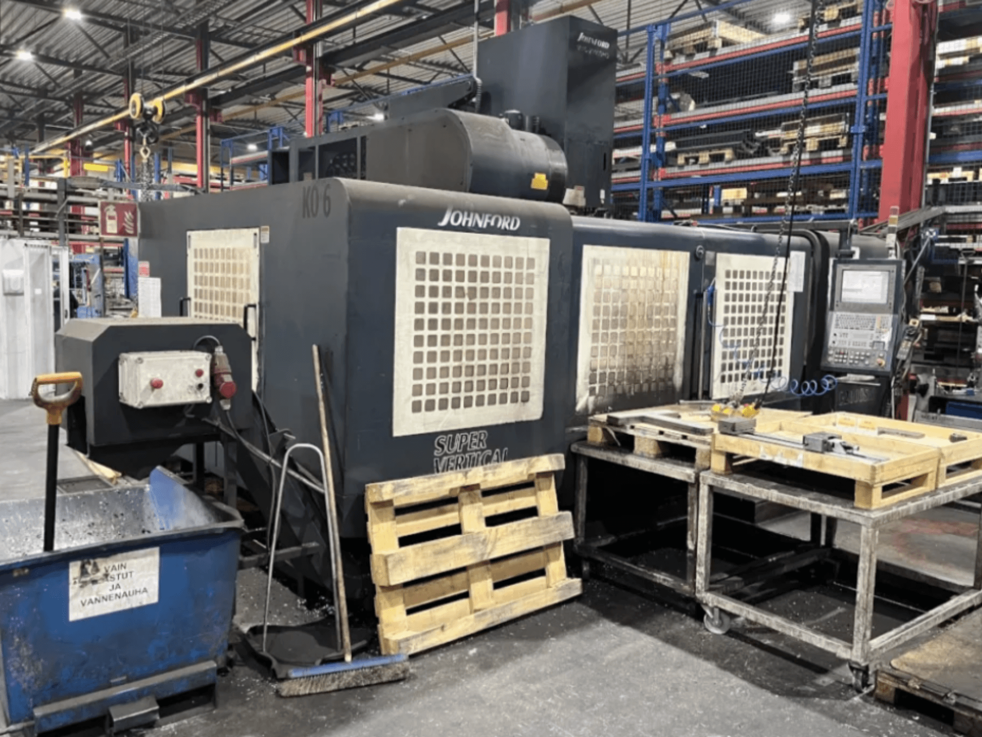 Johnford Super Vertikalna glodalica u tvornici, bočni pogled s upravljačkom pločom, paletama i opremom za čišćenje u blizini.