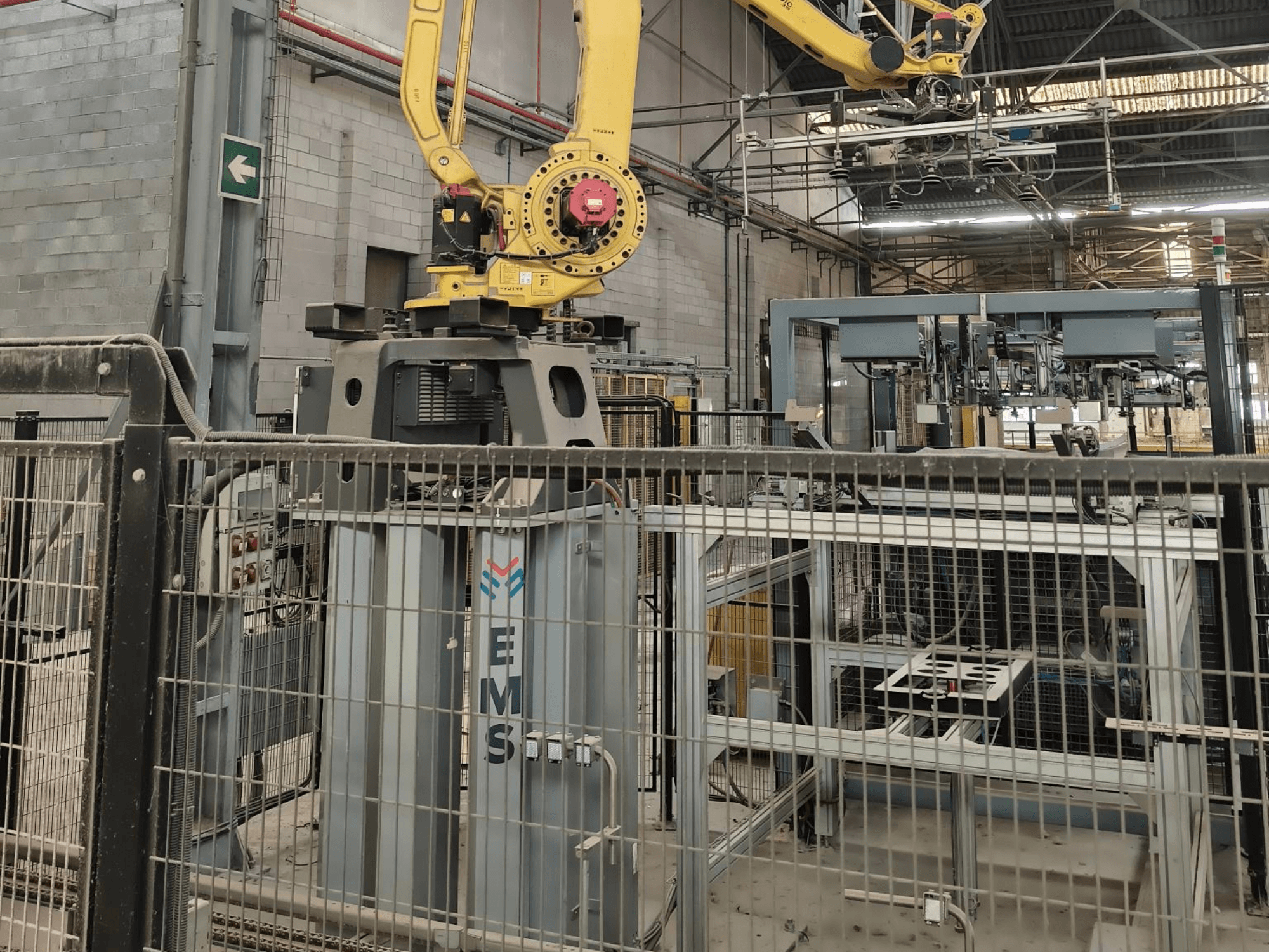 Prednji pogled na robotsku ruku FANUC M-410iC/315 postavljenu iznad EMS alata, s industrijskom opremom i ogradom u pozadini.