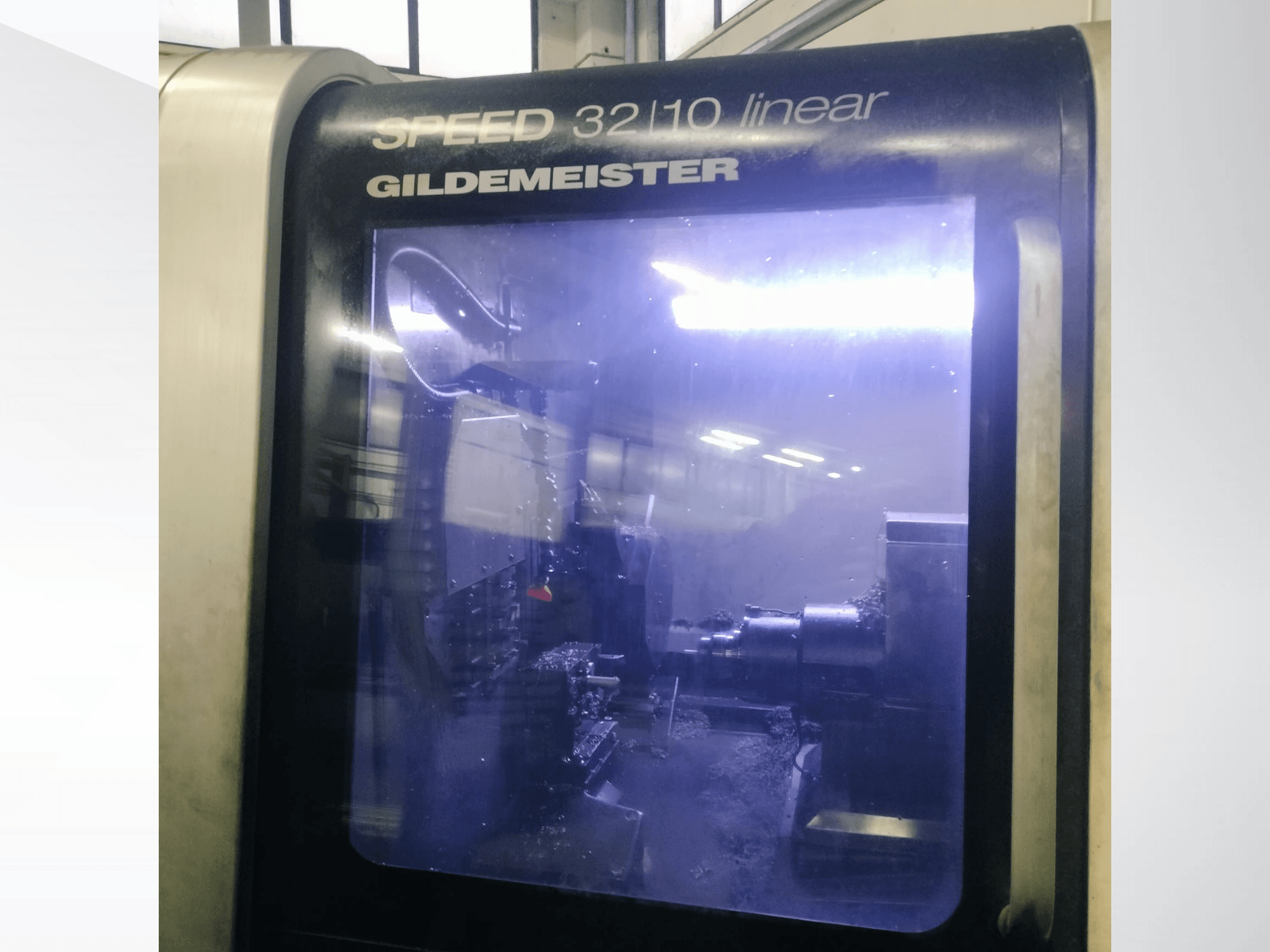 Prednji pogled na linearni CNC stroj Gildemeister SPEED 3210, s prikazom unutarnjih komponenti i tekućine za hlađenje u radu.