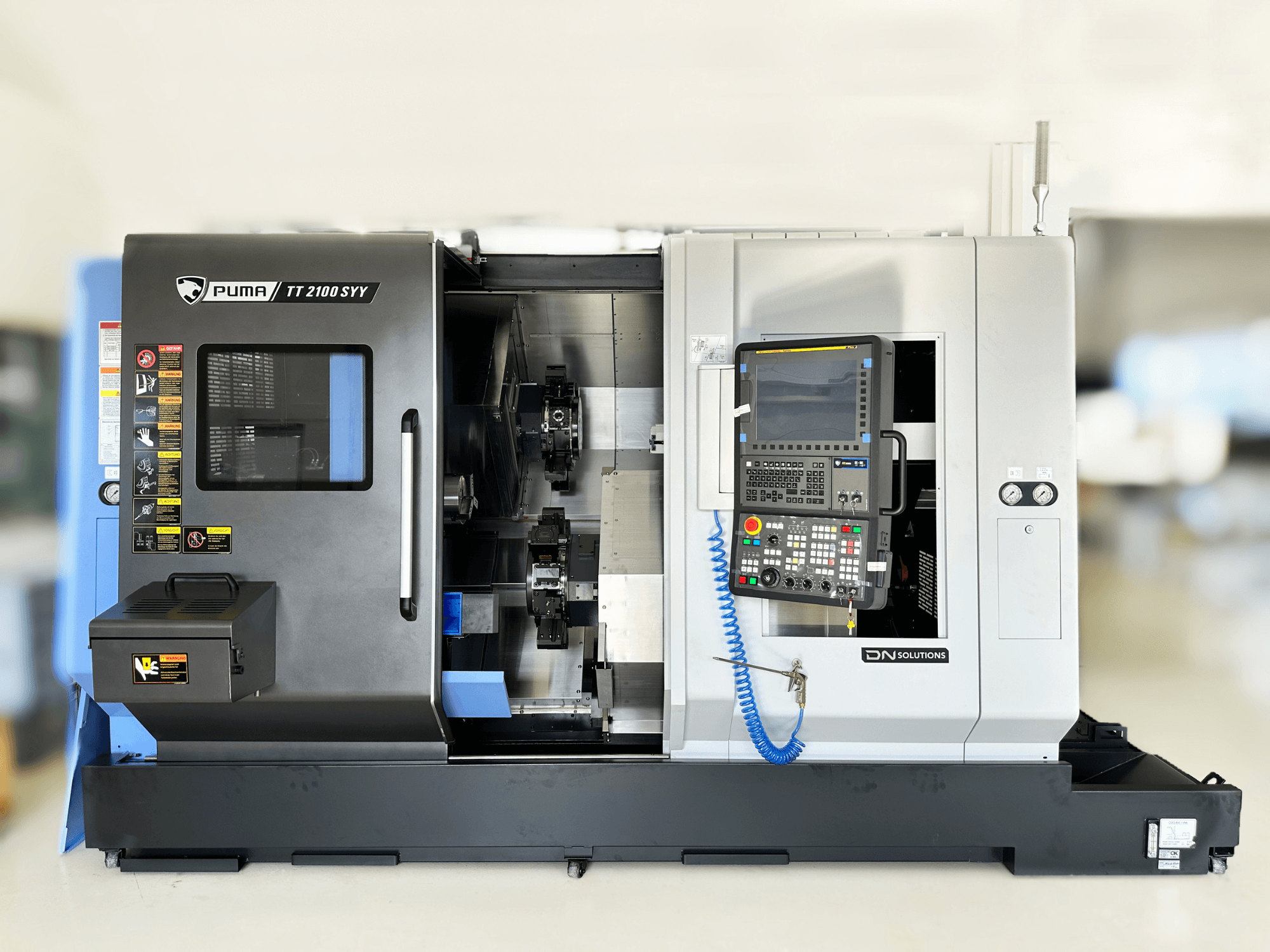 Prednji pogled na tokarsko-glodački centar DN SOLUTIONS PUMA TT2100SYY, s upravljačkom pločom i vidljivim unutarnjim komponentama.