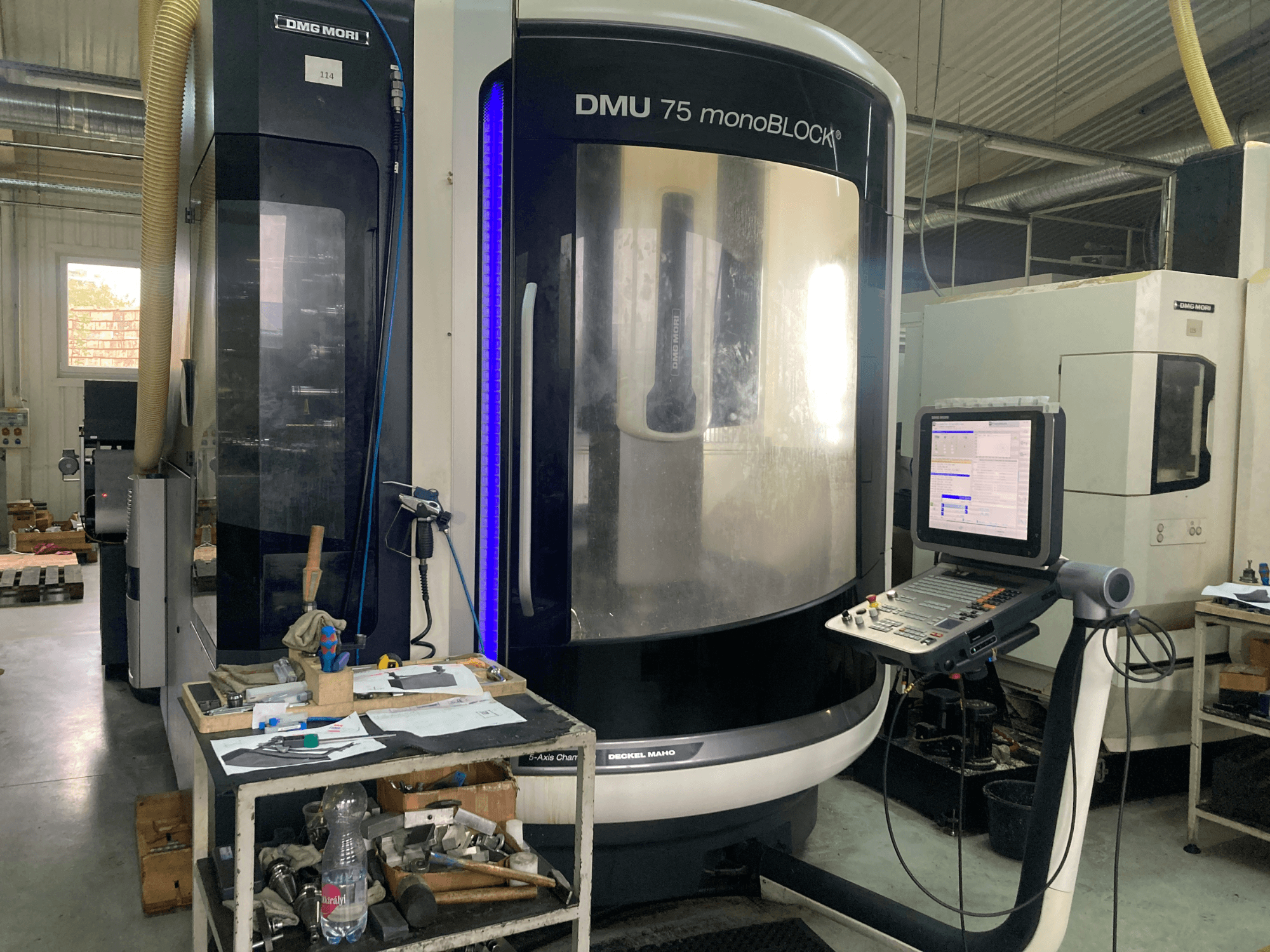 DMG MORI DMU 75 monoBLOCK® CNC stroj, prednji pogled, s upravljačkom pločom, alatima i radnim prostorom s materijalima.