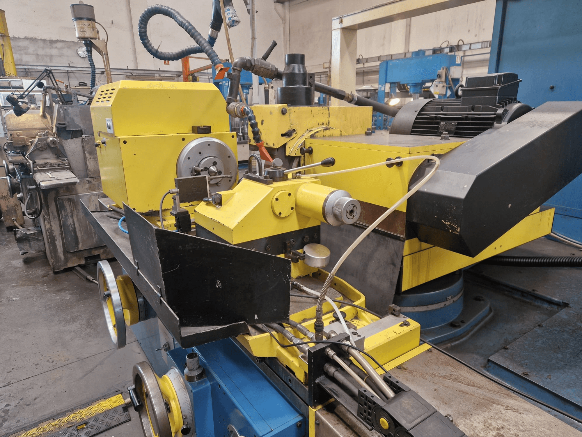 Žuti industrijski stroj s crnim dijelom, s brojčanikom i crijevima, gledan sprijeda pod blagim kutom.