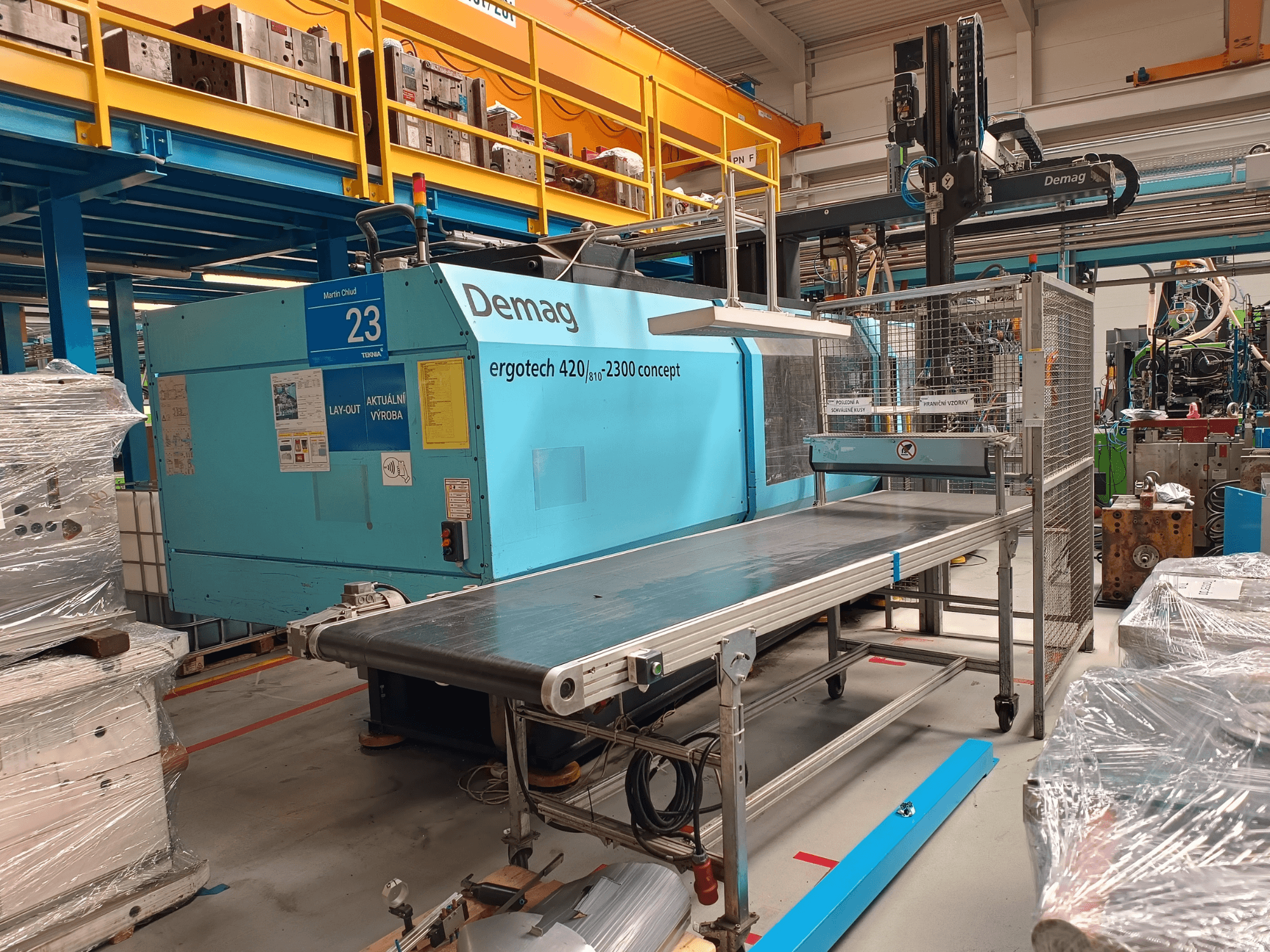 Bočni prikaz hidrauličkog stroja za brizganje plastike Demag ergotech 420/810 - 2300, s transporterom i sigurnosnim kućištem.