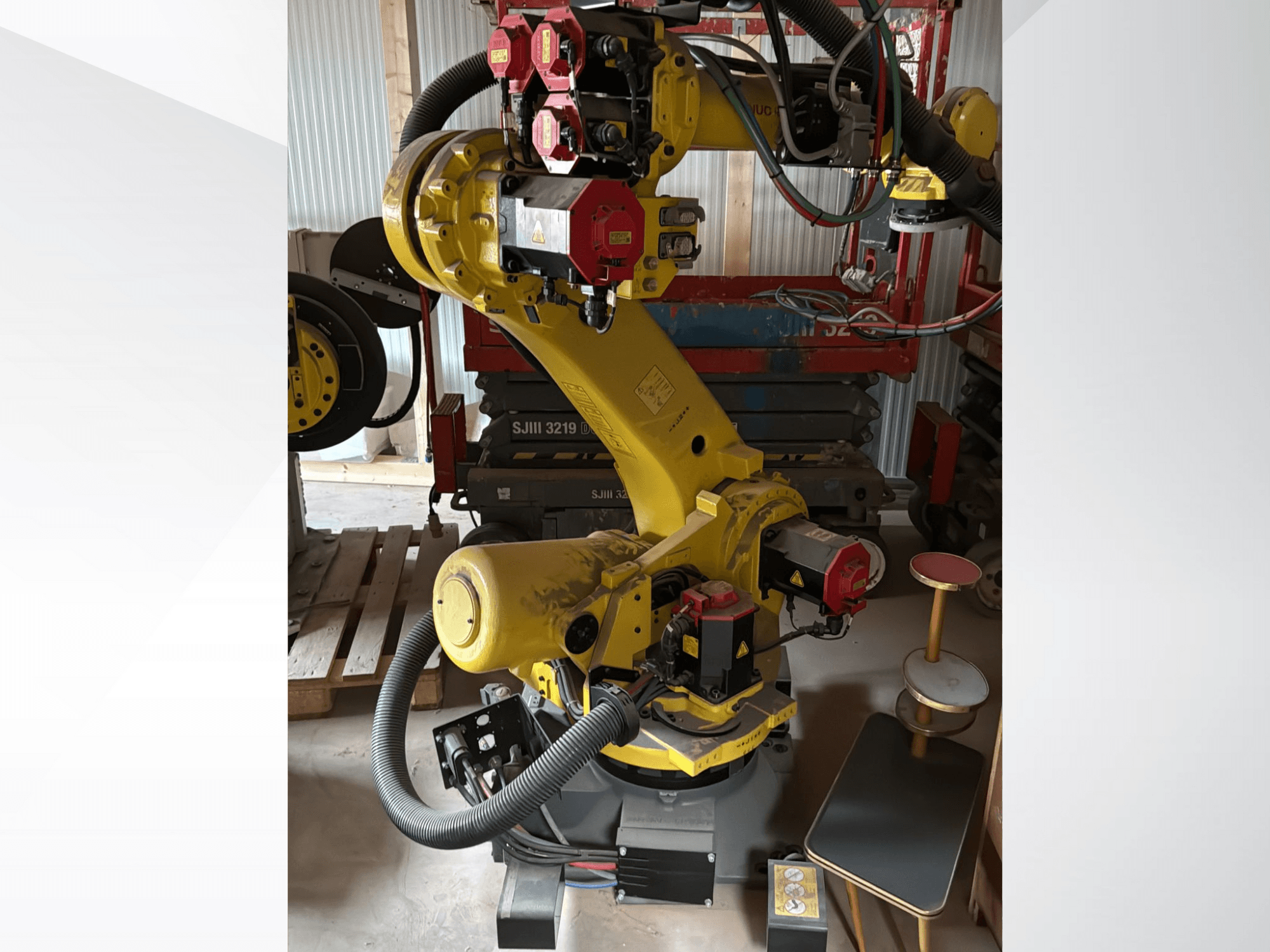 Žuta industrijska robotska ruka s crvenim kontrolerima, prednji pogled; ima više zglobova i crijeva, postavljena na radnom mjestu.