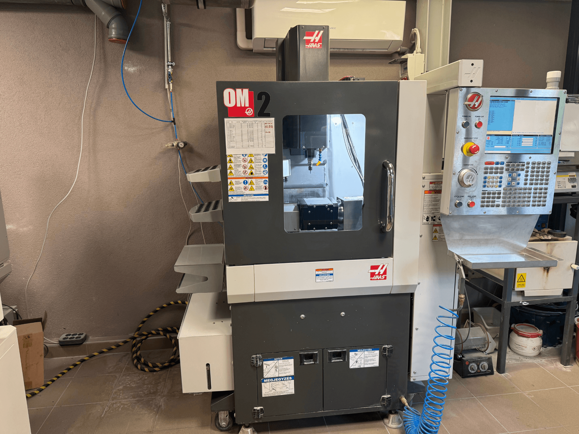 Haas OM-2 CNC stroj, prednji pogled, sadrži upravljačku ploču, vreteno i sigurnosne naljepnice, smješten u radioničkom okruženju.