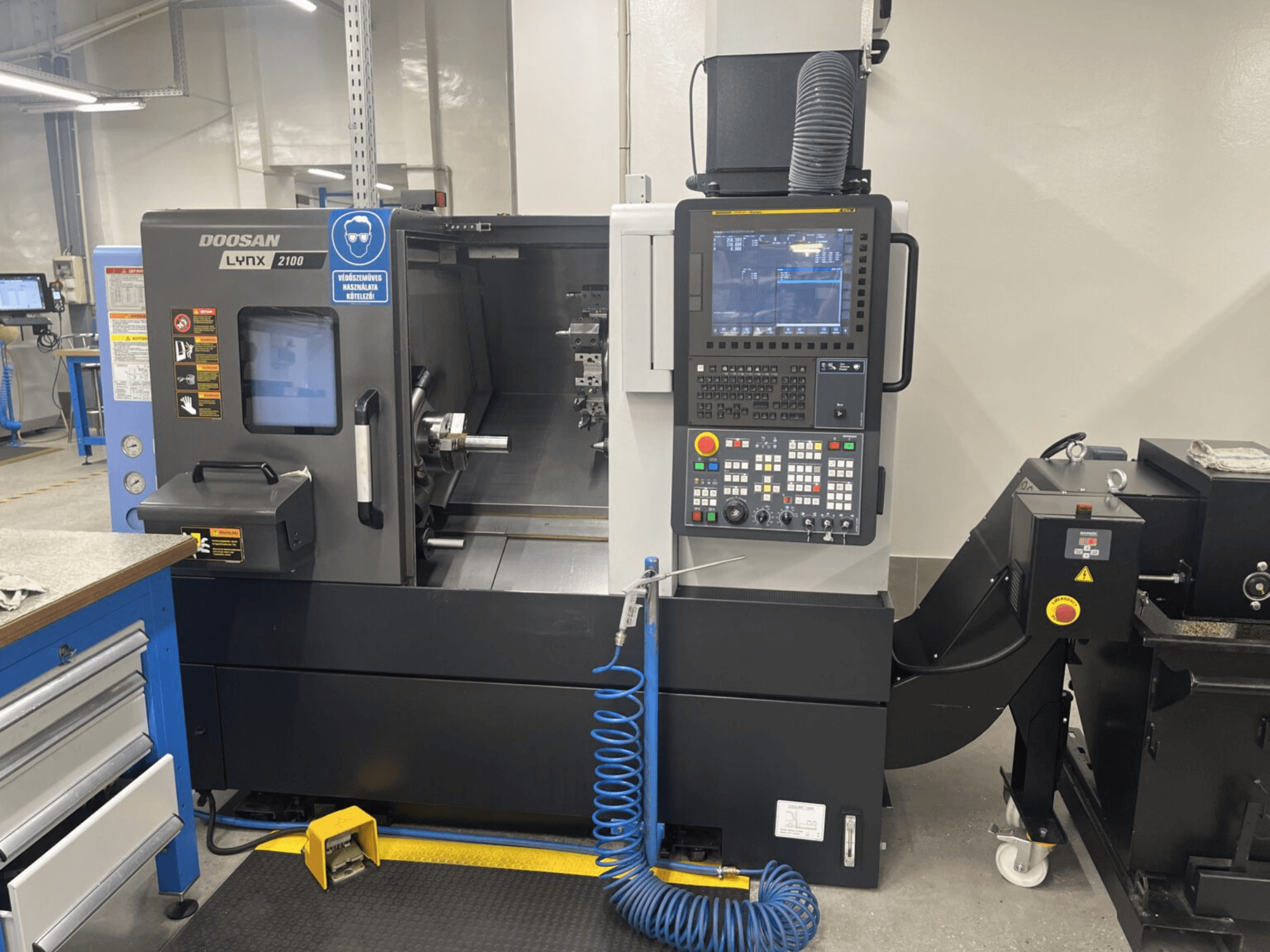 Prednji pogled na horizontalni tokarski stroj DOOSAN Lynx 2100A, s prikazom upravljačke ploče i područja vretena s istaknutim sigurnosnim značajkama.