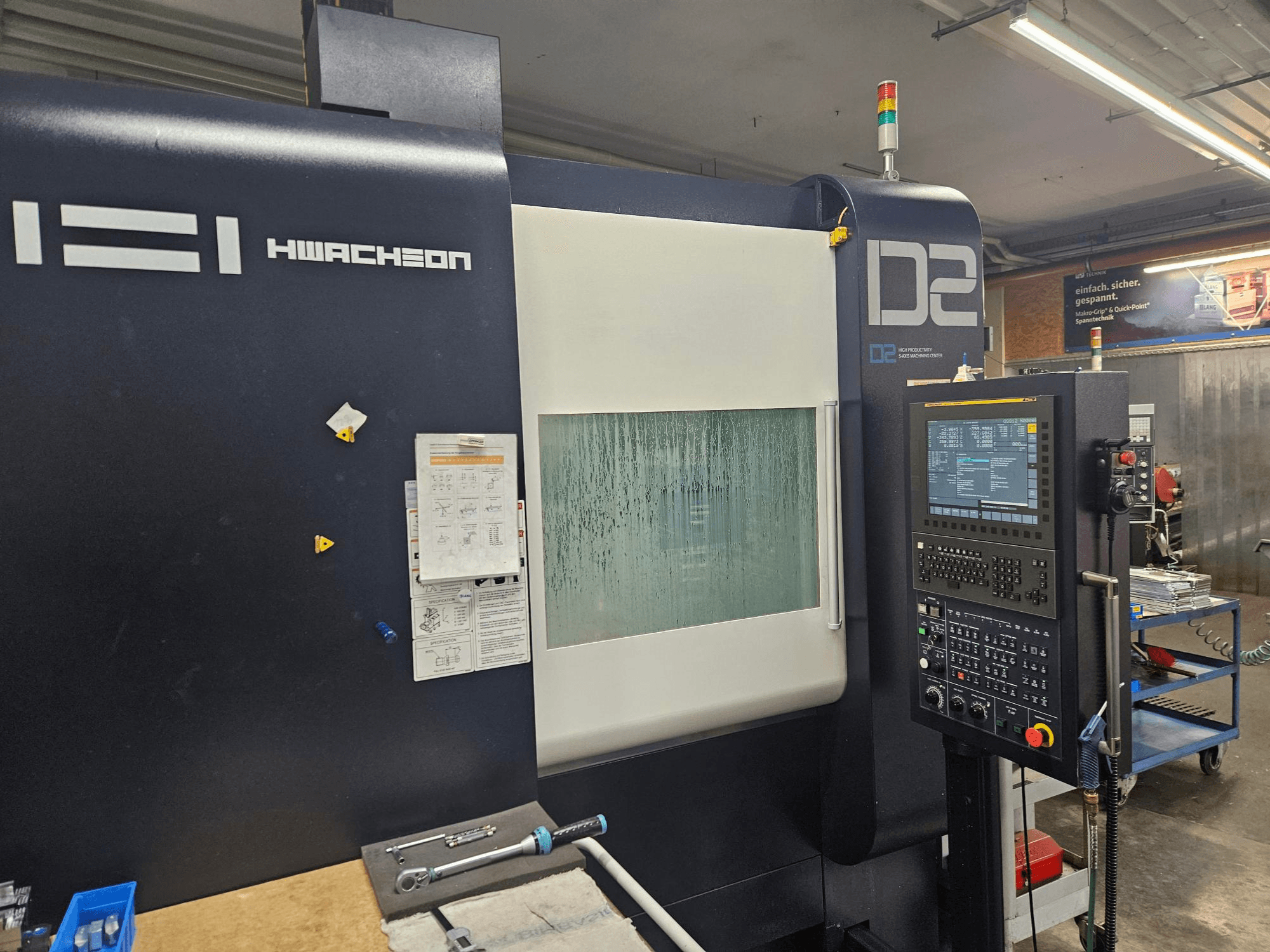 Vertikalni obradni centar HWACHEON D2-5AX 12k, prednji pogled s upravljačkom pločom i zamagljenim prozorčićem za pregled.