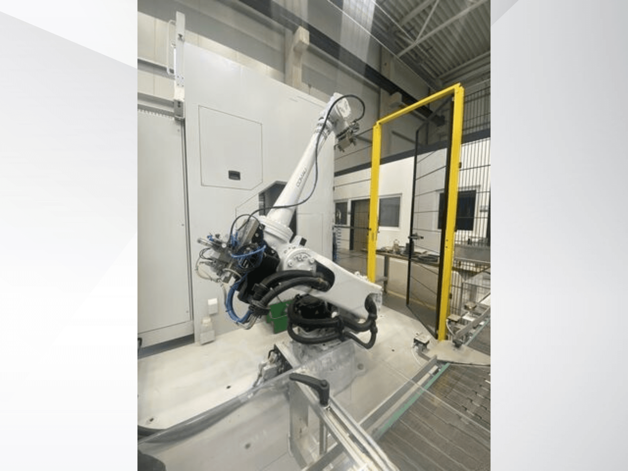 Robotska ruka COMAU Smart NJ 40-2.5 u bočnom pogledu, s kabelima i žutim sigurnosnim vratima u tvorničkom okruženju.