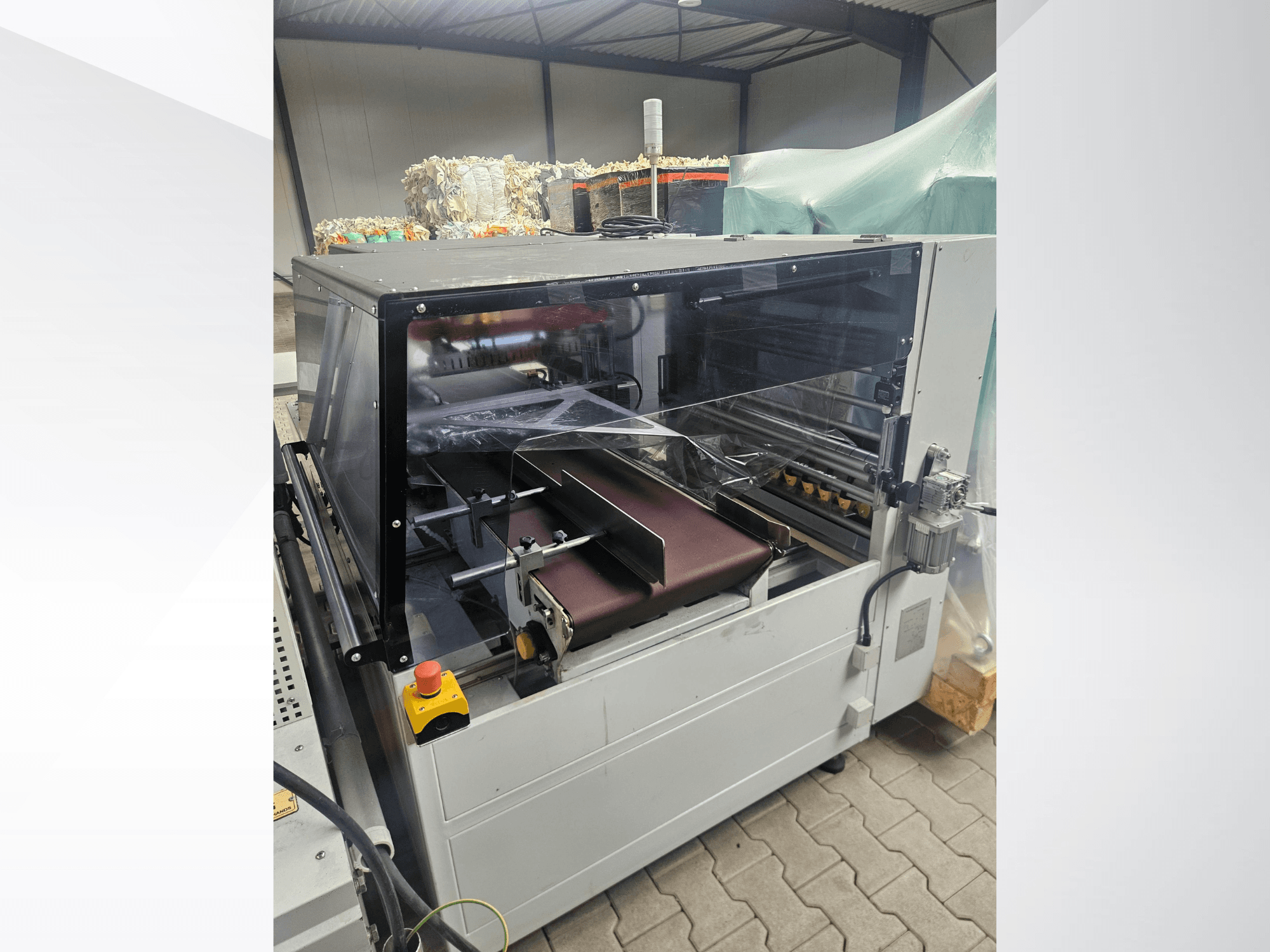 AMTEC Speed Shrink 40 PRO stroj, pogled sprijeda, prikazuje mehanizam za obradu plastike s prozirnim sigurnosnim poklopcem i transportnom trakom.