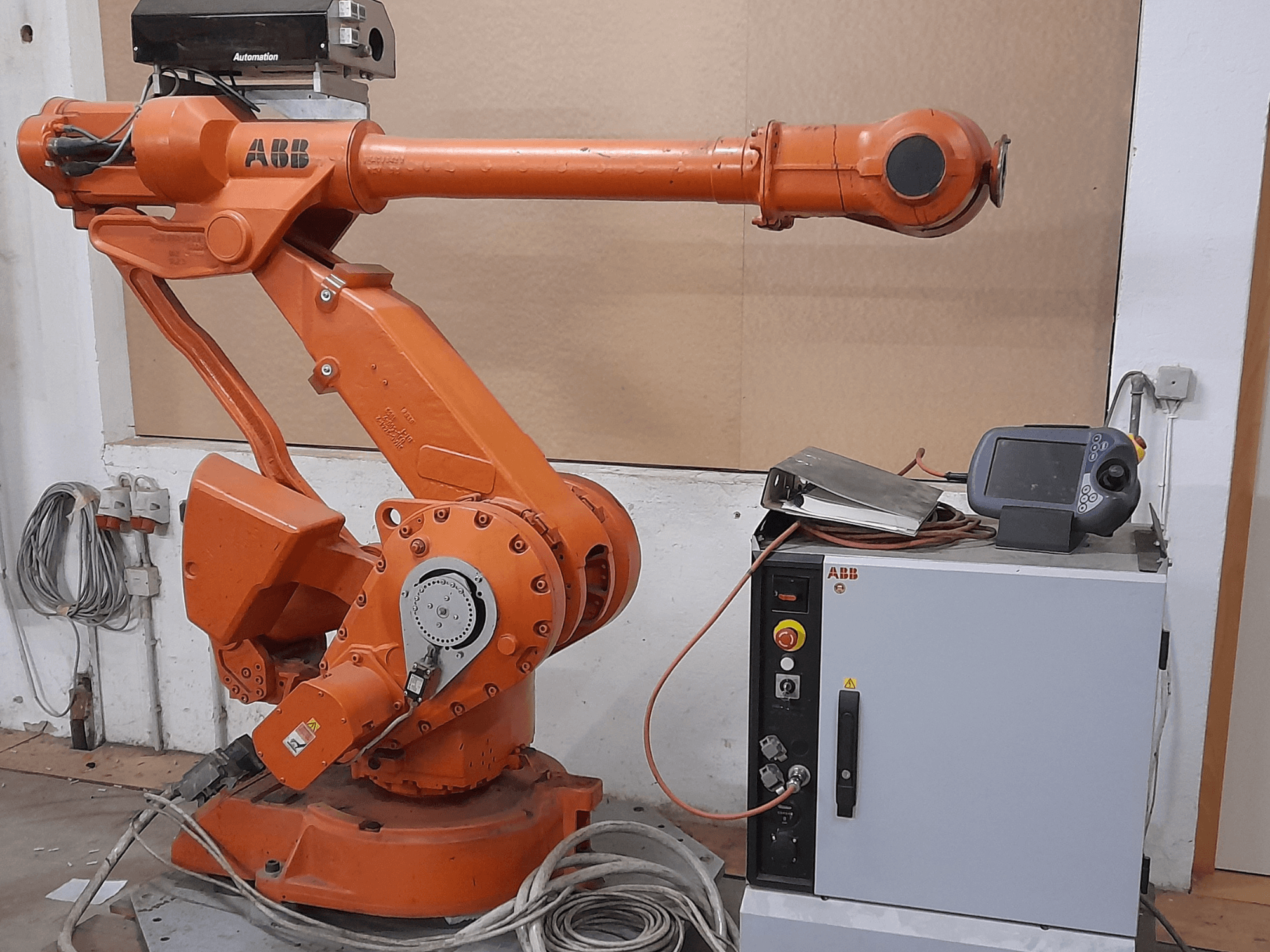 Narančasta ABB robotska ruka s upravljačkom pločom, prednji pogled, s prikazom kabela i opreme za automatizaciju.