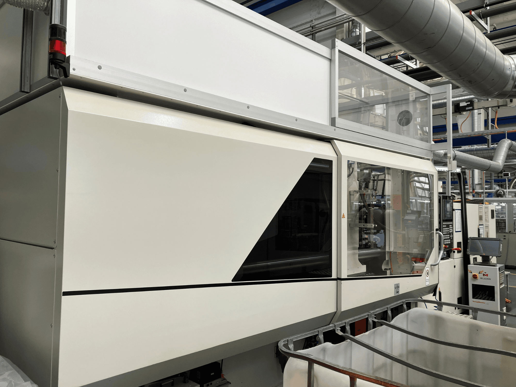 Prednji pogled na industrijski stroj s elegantnim bijelim dizajnom, zaslonom i staklenim dijelom za vidljivost komponenti.