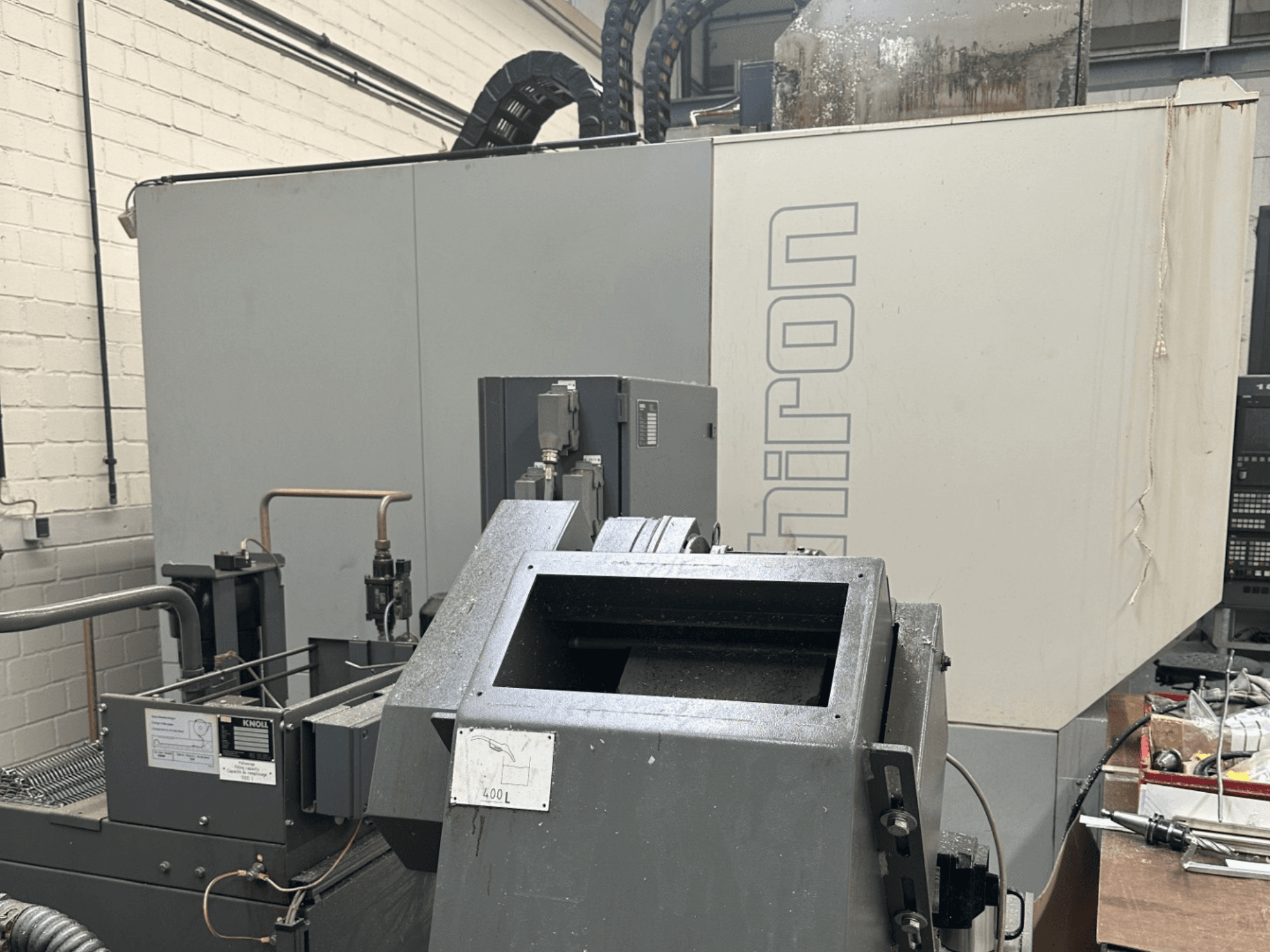 MARKA: Chiron; Prednji pogled na industrijski CNC stroj sa sivom vanjštinom, vidljivom upravljačkom pločom i komponentama stroja u fokusu.