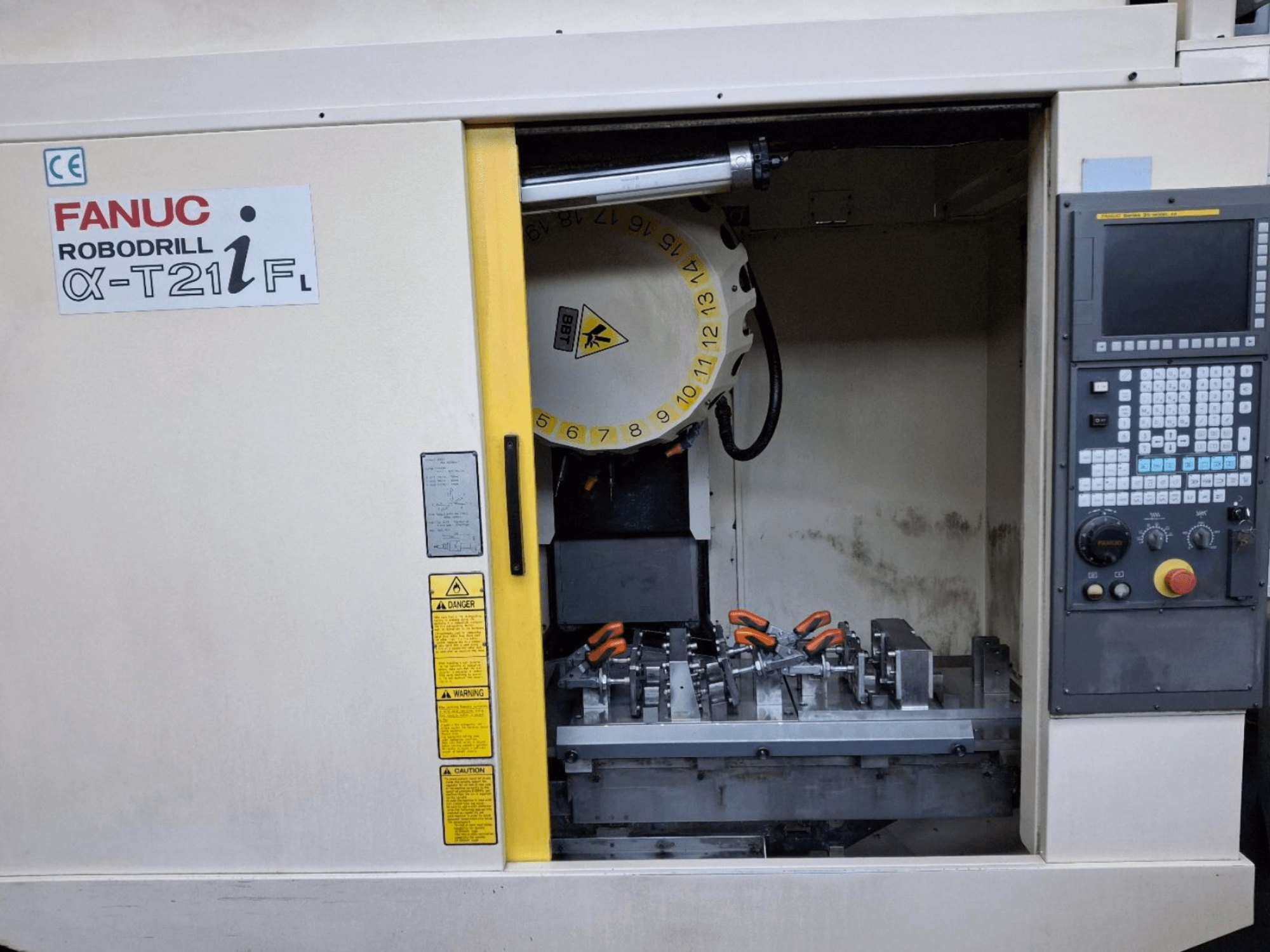 Prednji pogled na vertikalni obradni centar FANUC ROBODRILL α-T21iFL, s alatima i upravljačkim elementima unutar ormara stroja.