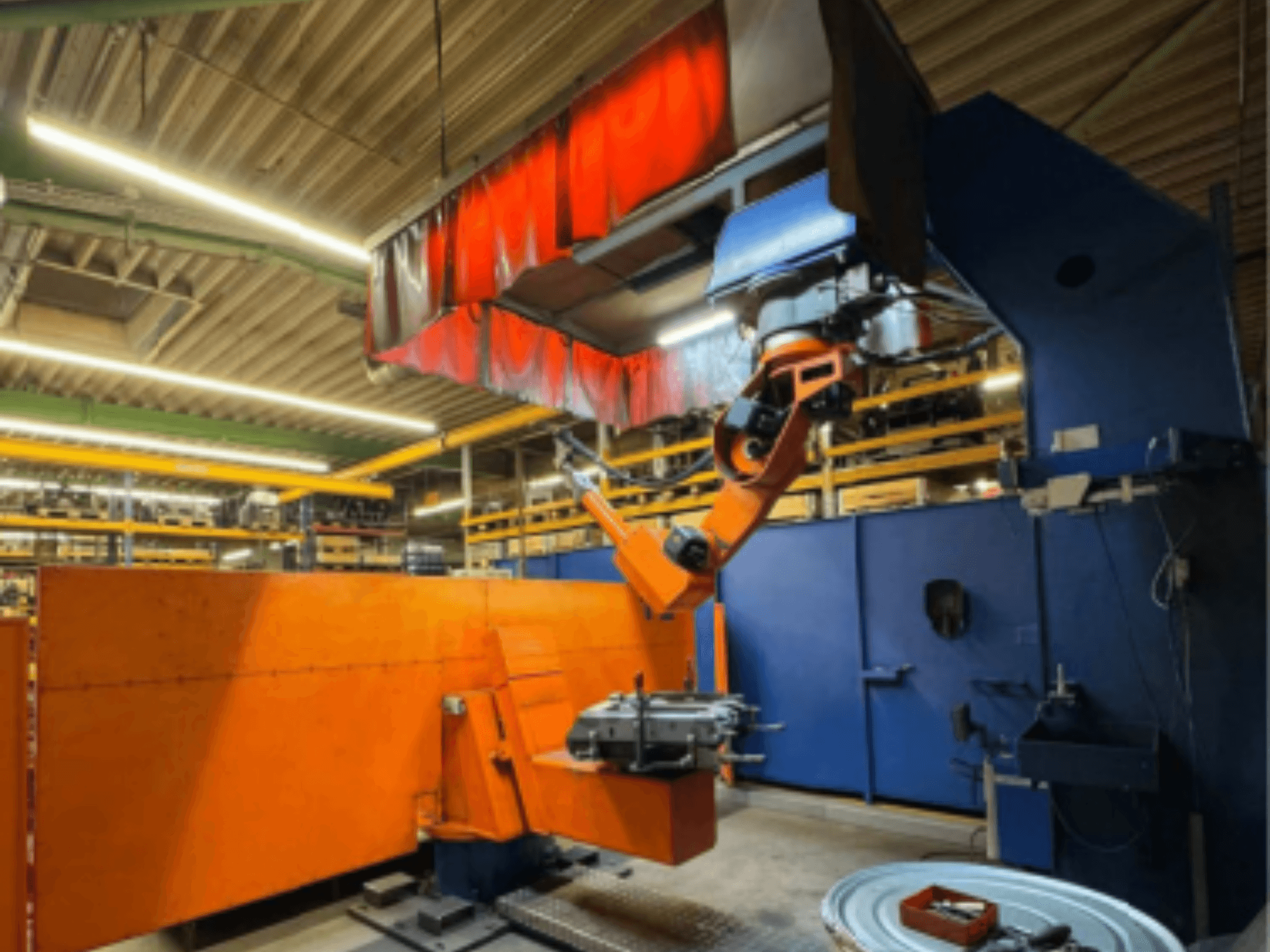 Robot za zavarivanje CLOOS Romat 350 e u industrijskom okruženju, prednji pogled s narančastom rukom, drži obradak ispod zavjese iznad glave.