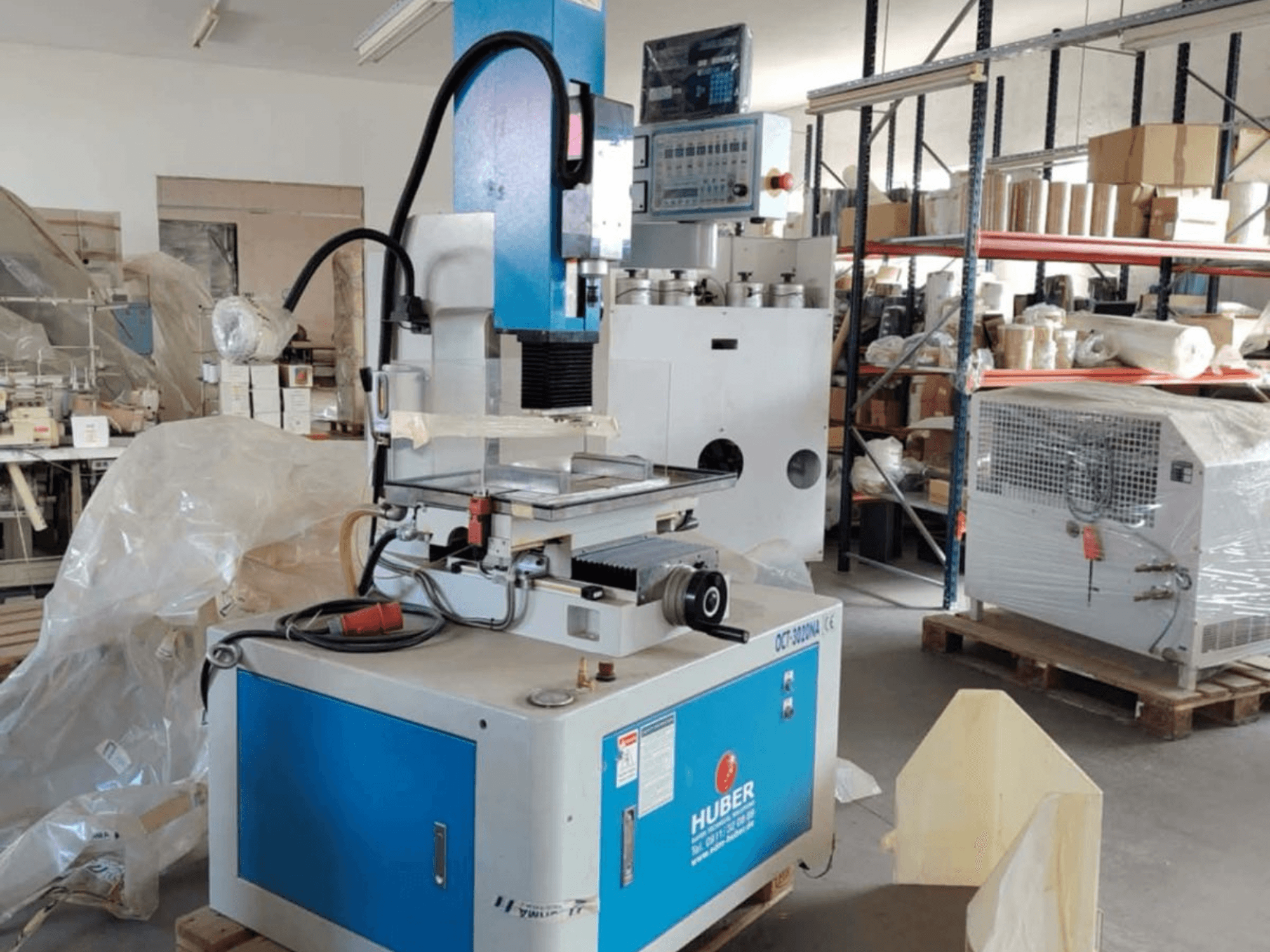 HUBER OCT-3020 NA stroj za eroziju u radionici, prednji pogled koji prikazuje plavo i sivo kućište, digitalne kontrole i radno područje.