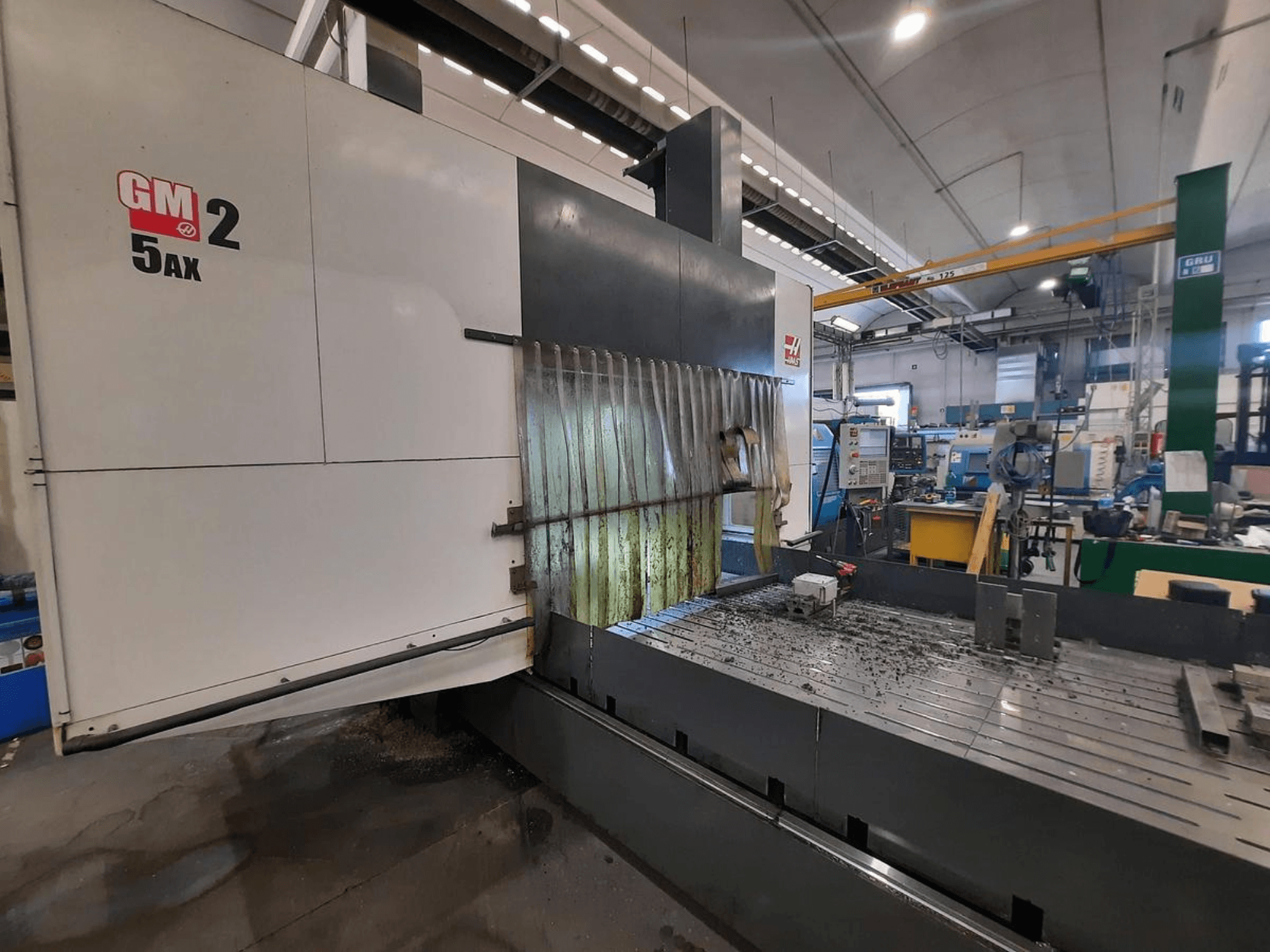 CNC stroj GM 2 5AX u radionici, bočni pogled, prikazuje radno područje i metalne strugotine na površini kreveta.