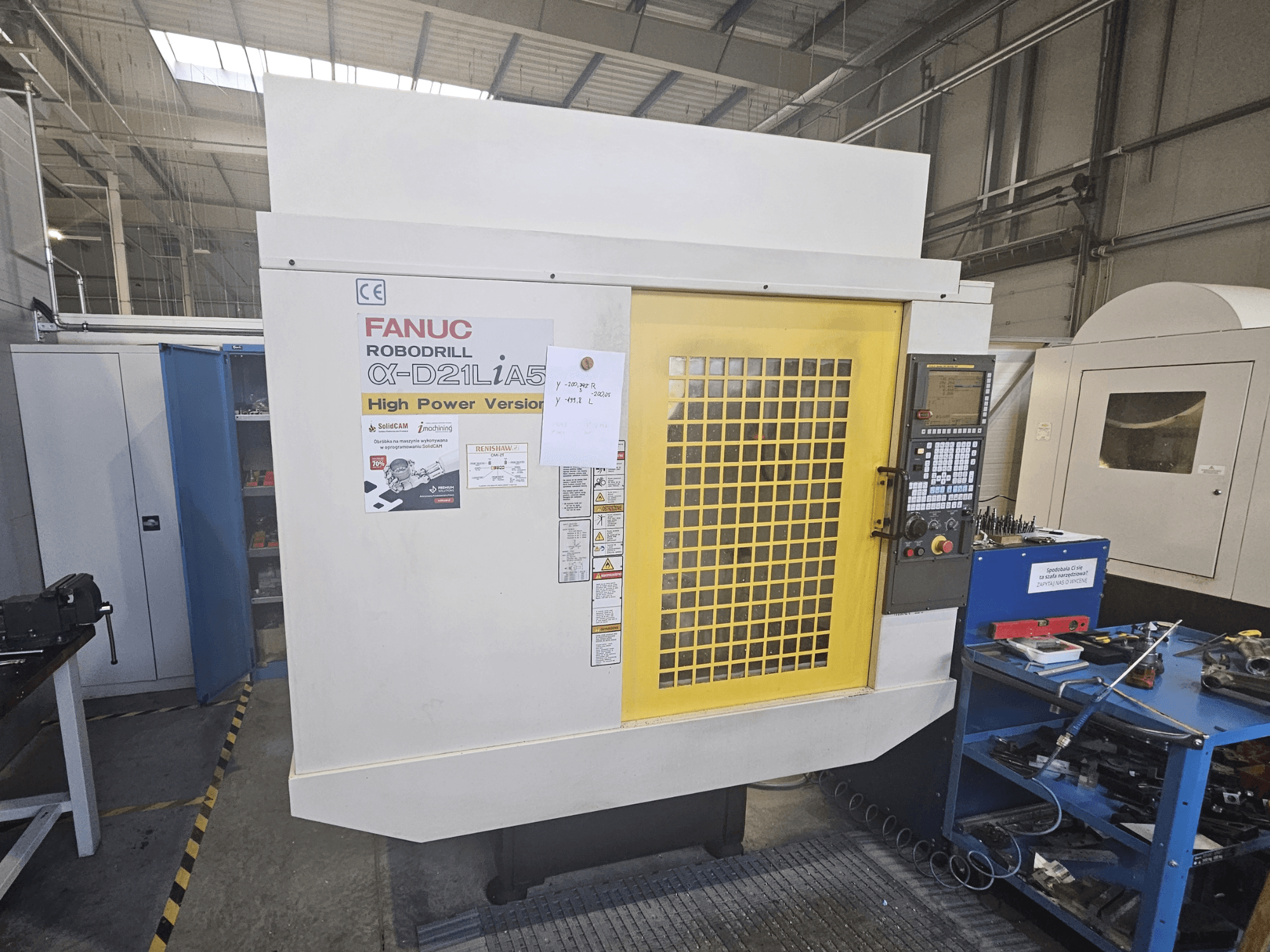 Prednji pogled na FANUC Robodrill α-D21LiA5 sa žutim sigurnosnim vratima, upravljačkom pločom i alatima radnog prostora u blizini.